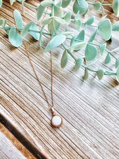 Handgemachte weiße Jade-Kette mit rundem Anhänger in Gold,  liegend auf Holz