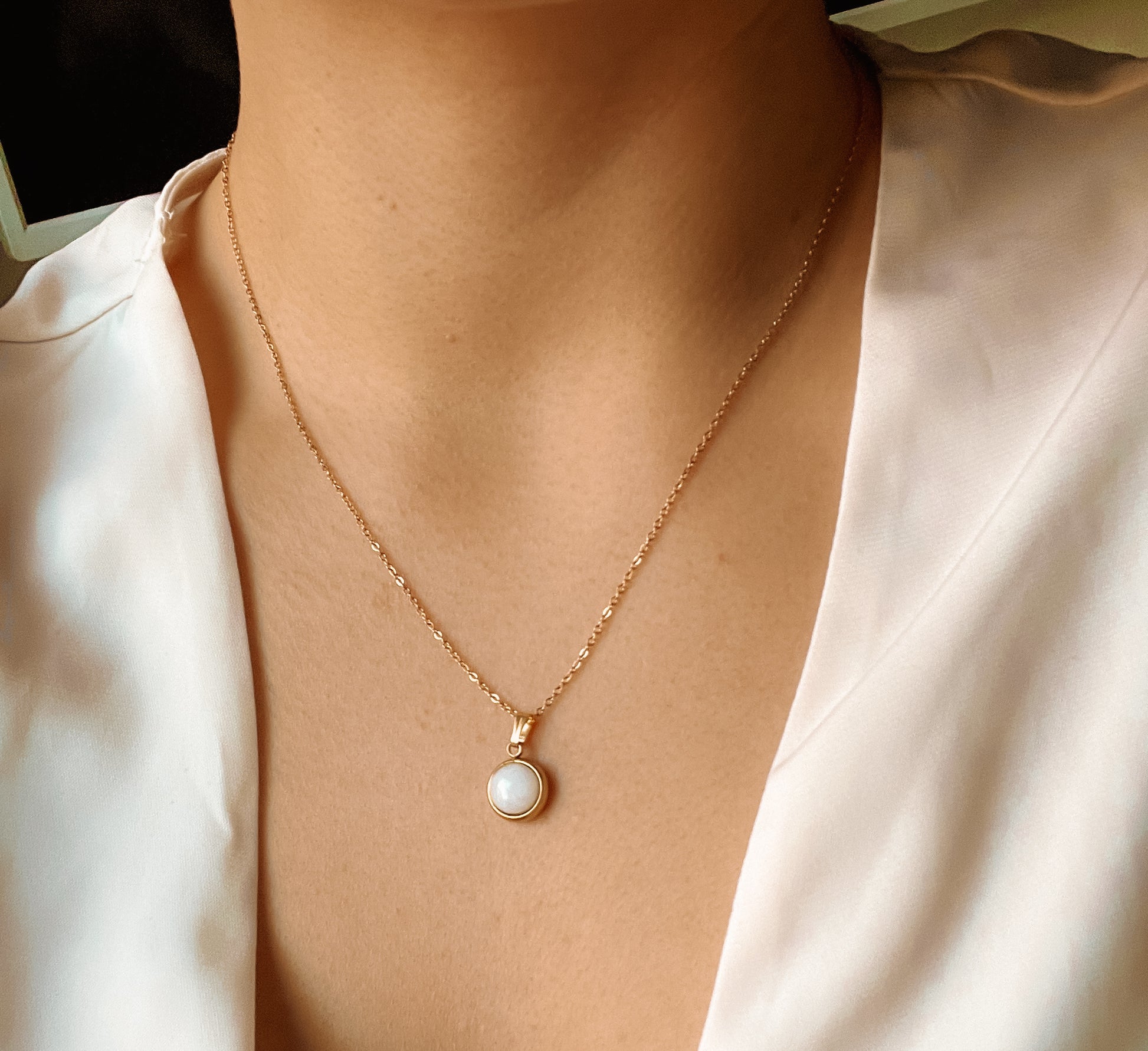 Runder weißer Jade-Anhänger an feiner Goldkette, am Hals eines Modells gezeigt.