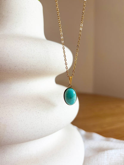 Kette mit goldenem ovalen Anhänger mit hellblauem Amazonit Stein hängend an einer Vase