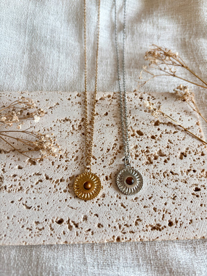 Ketten mit runden Medaillon Anhängern mit braunen Tigerauge Steinen in Gold und Silber auf Steinplatte