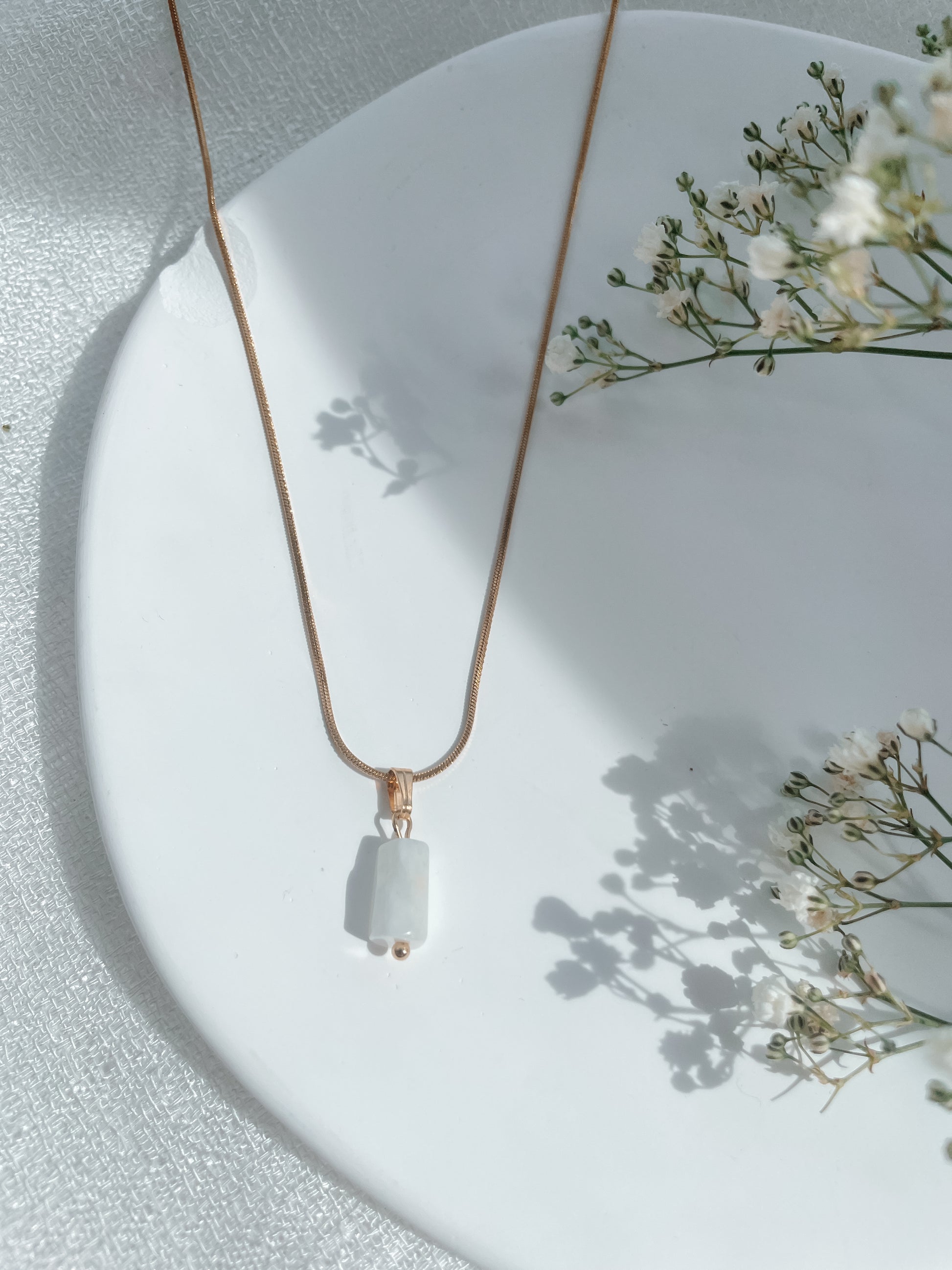 Handgemachte weiße Mondstein-Kette mit Naturstein Anhänger in Gold,  liegend auf Tablett mit Blumen