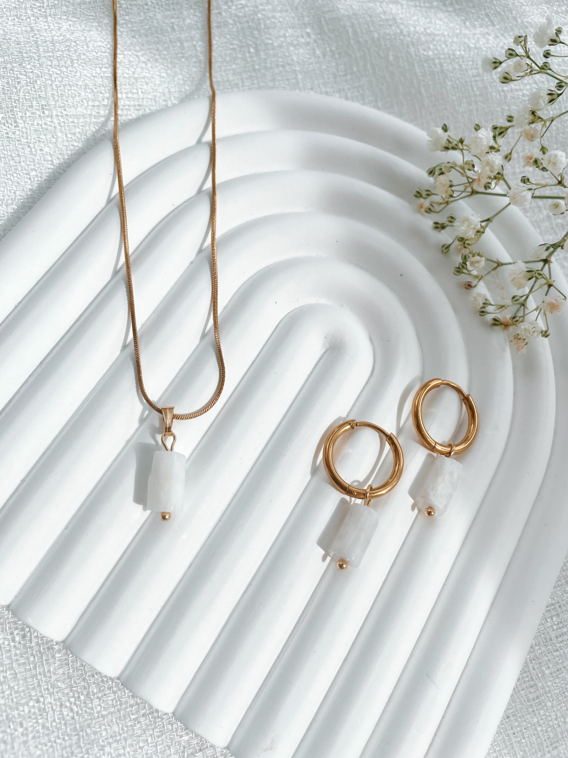 Goldenes Schmuckset mit Ohrring und Halskette mit weißen Mondstein Anhängern liegend auf weißem Tablett
