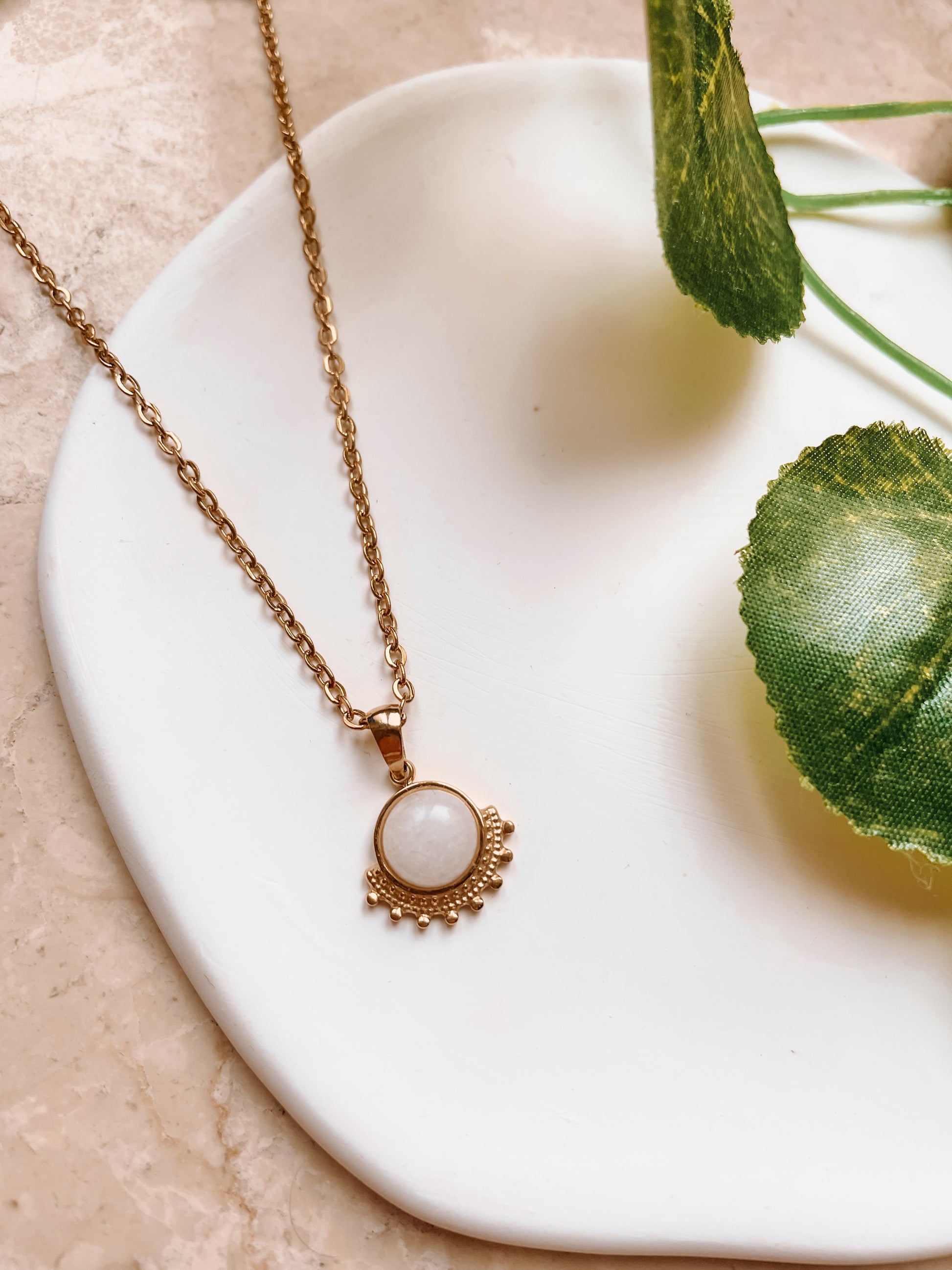 Handgemachte weiße Jade-Kette mit rundem Anhänger in Gold mit Zacken,  liegend auf Tablett