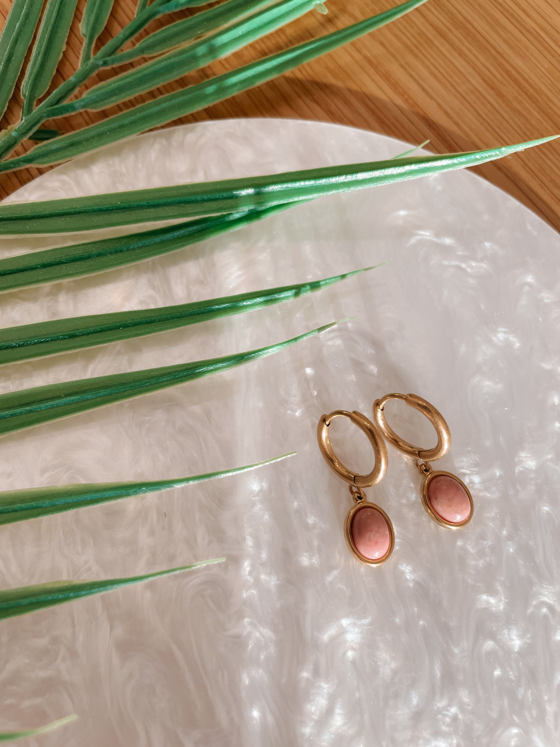 Goldene Creolen-Ohrringe mit ovalen, rosa Rhodonit-Steinen auf Tablett