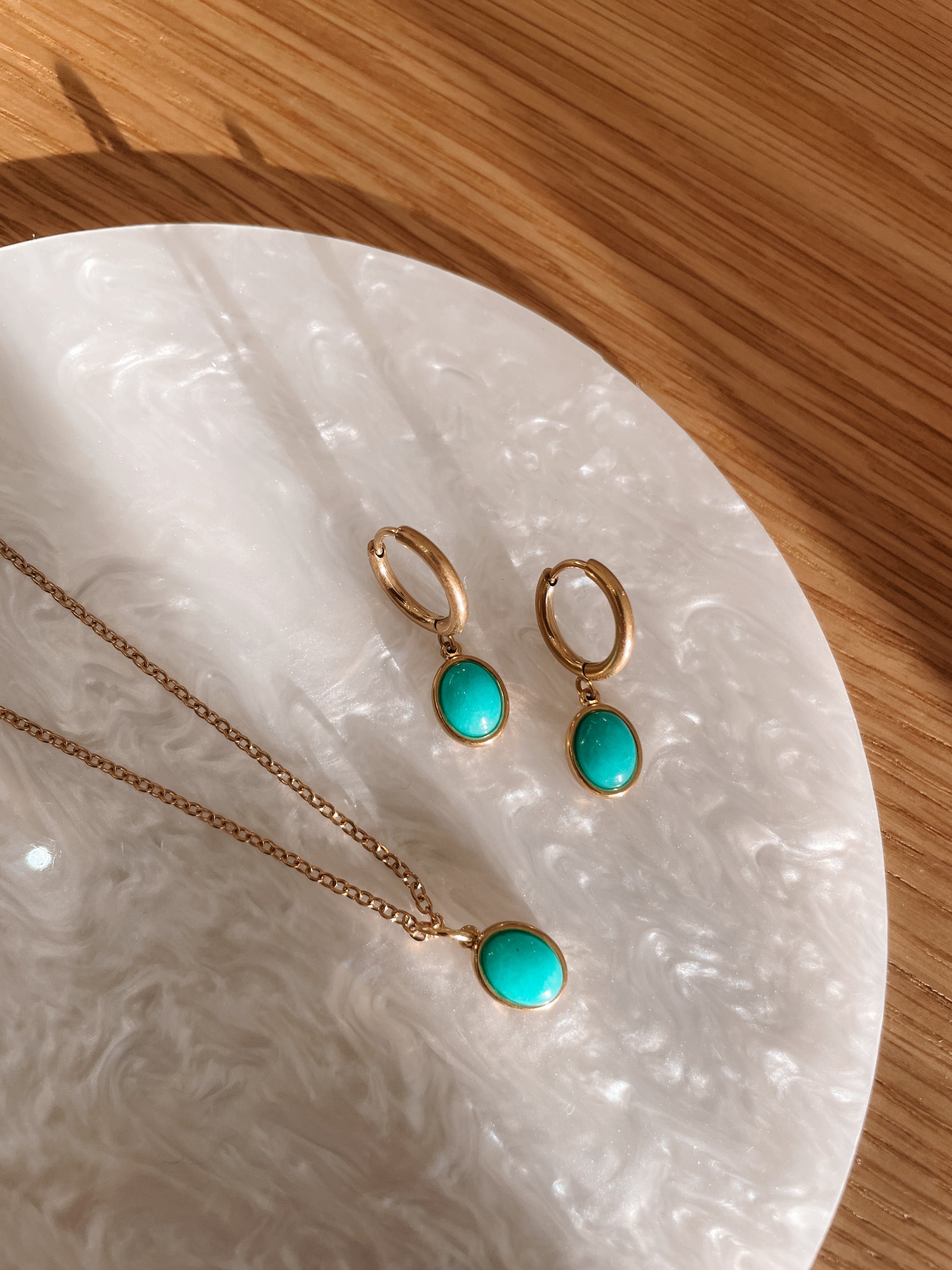 Goldenes Schmuckset mit Ohrring und Halskette mit blau-grünem Amazonit Anhängern liegend auf Stein