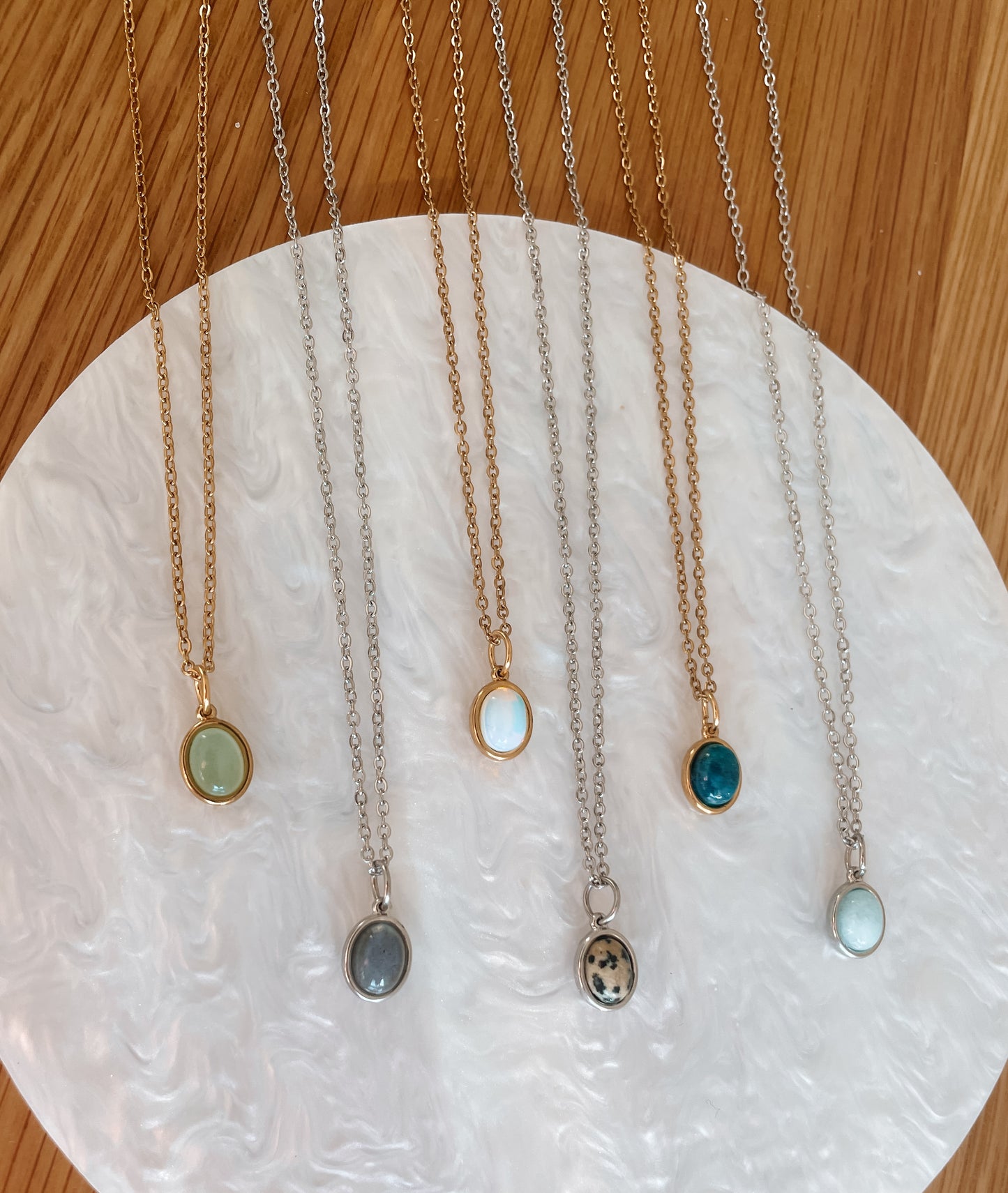 Handgemachte Edelstein-Ketten mit ovalem Anhänger in Gold und Silber, liegend auf Tablett.