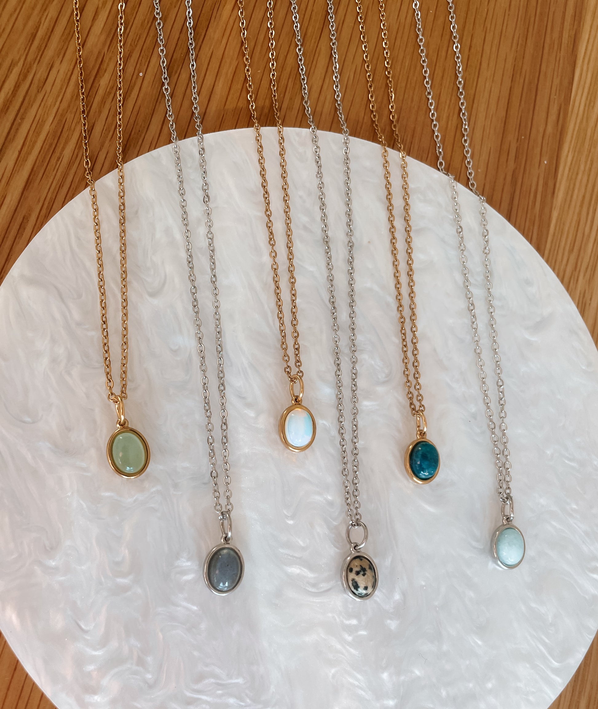 Handgemachte Edelstein-Ketten mit ovalem Anhänger in Gold und Silber, liegend auf Tablett.