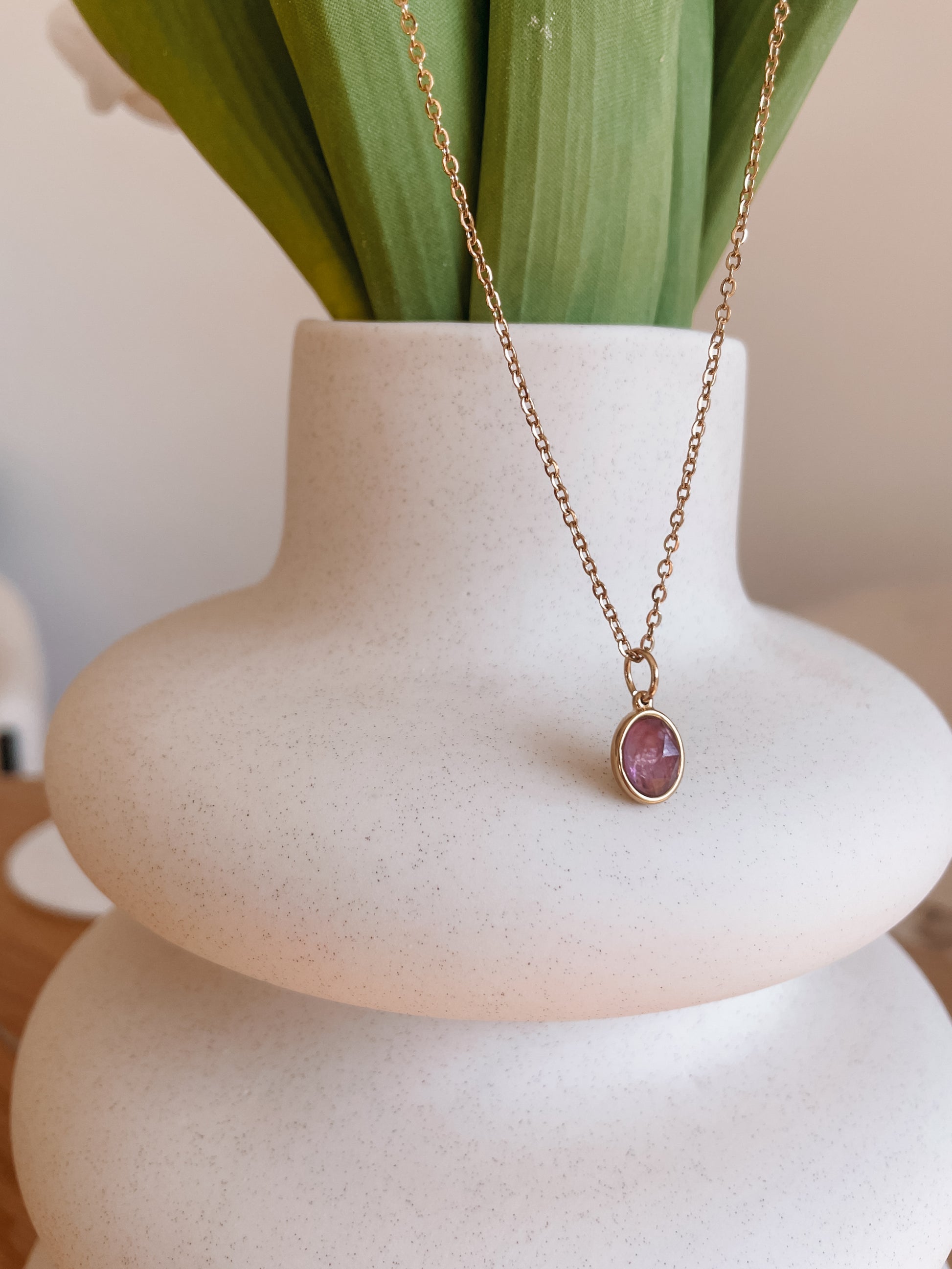 Handgemachte lila Amethyst-Kette mit ovalem Anhänger in Gold, hängend an einer Vase
