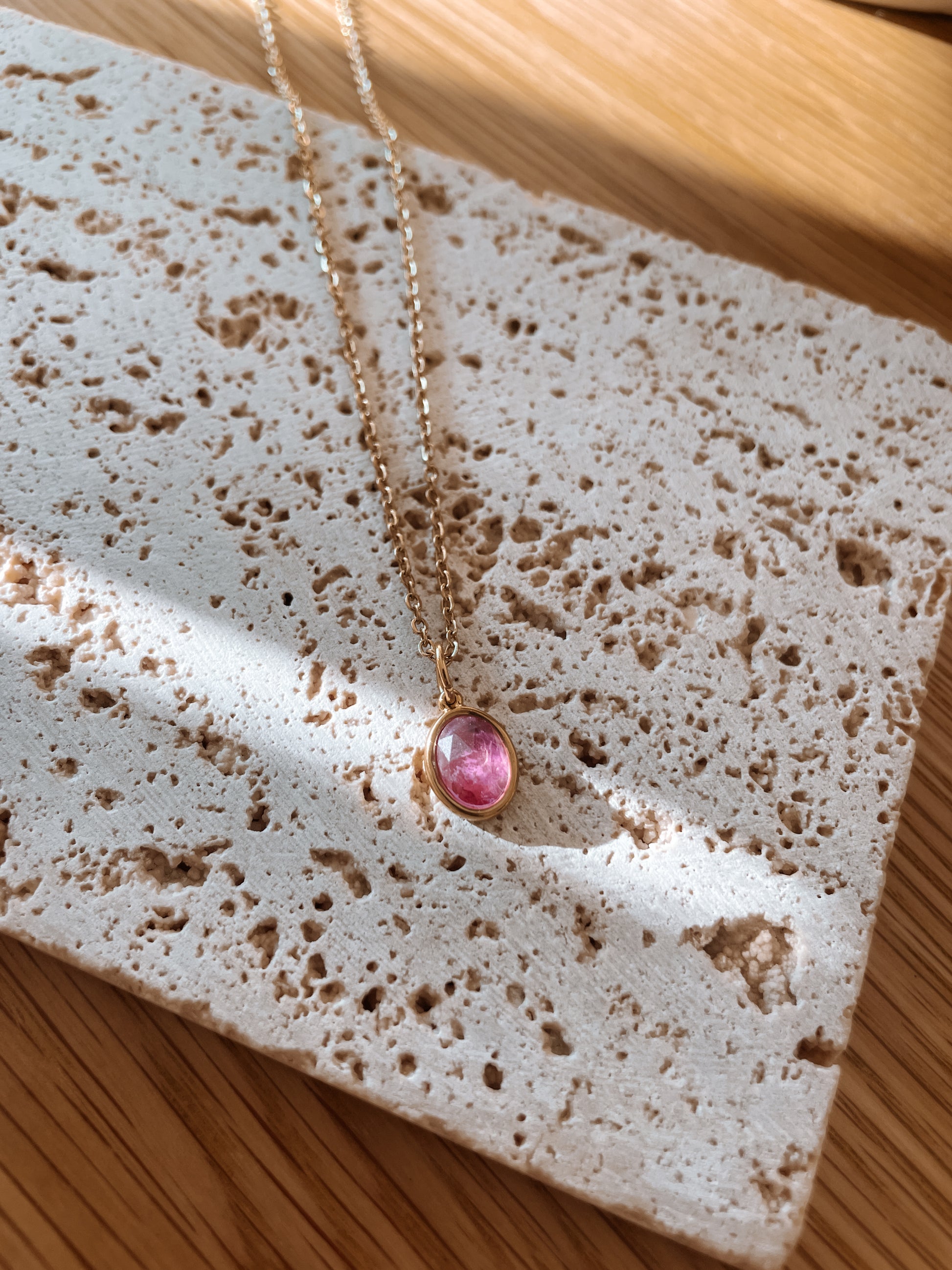 Handgemachte lila Amethyst-Kette mit ovalem facettierten Anhänger in Gold,  liegend auf Stein