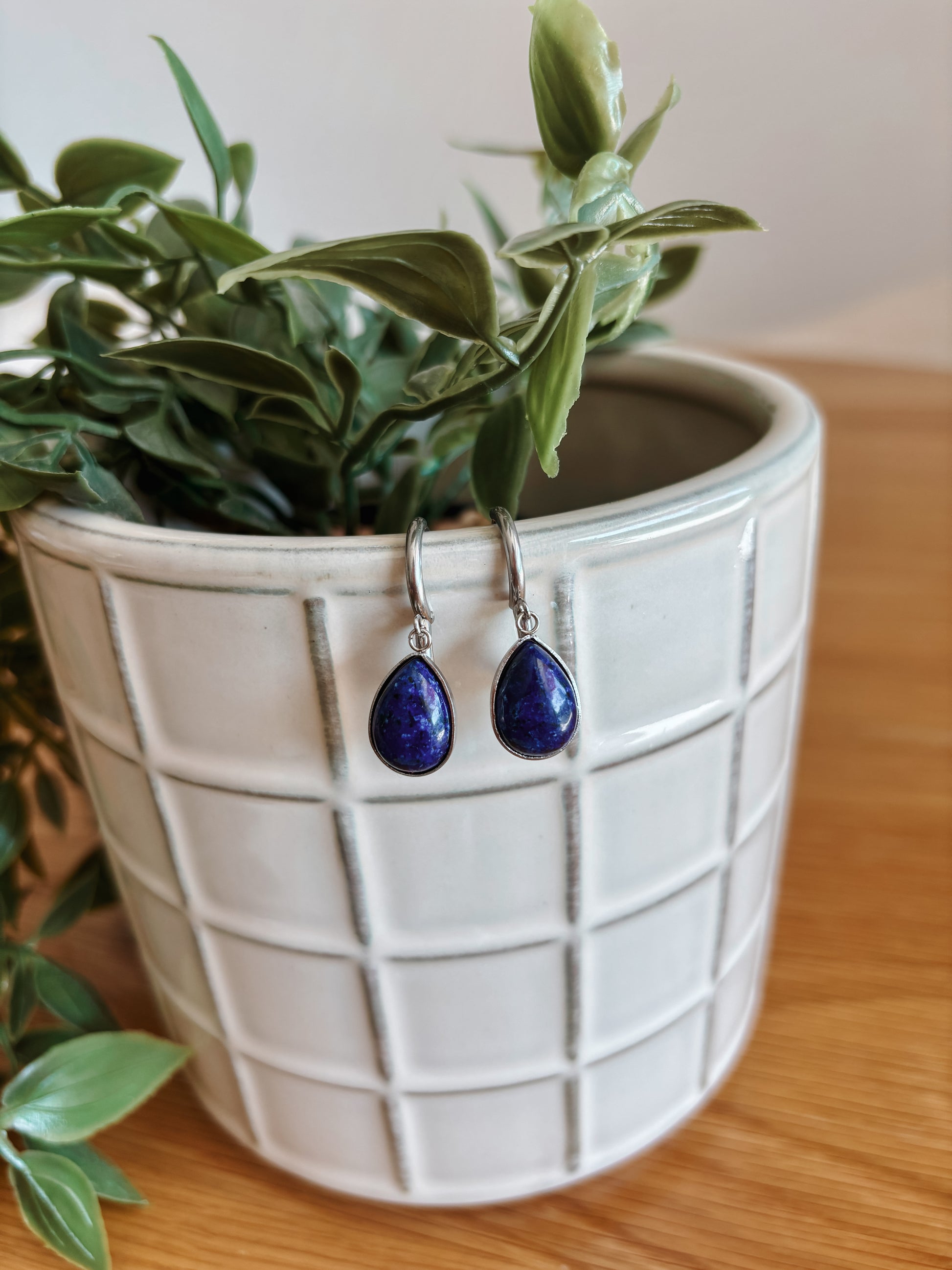 Silberne Creolen-Ohrringe mit tropfenförmigen, blauen Lapislazuli-Steinen hängend an Vase