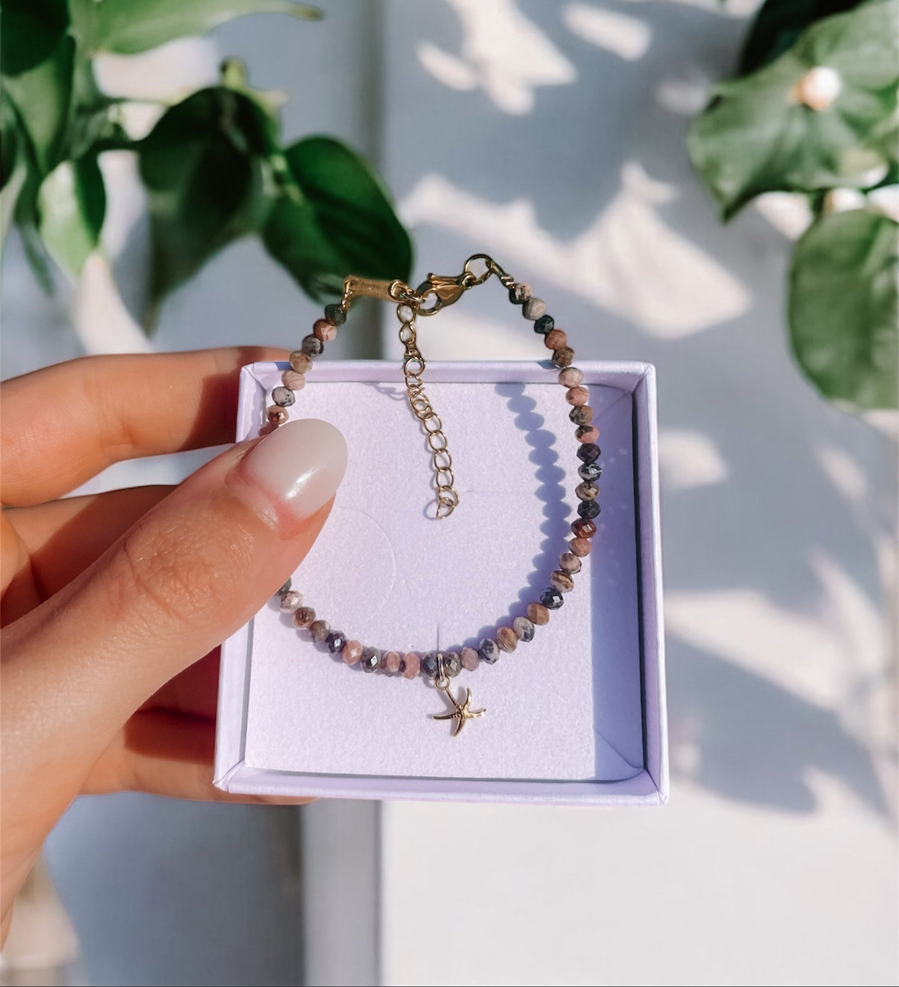 Rosa Braunes Rhodonit-Perlenarmband in Gold mit Seestern Anhänger in einer weißen Schmuckbox