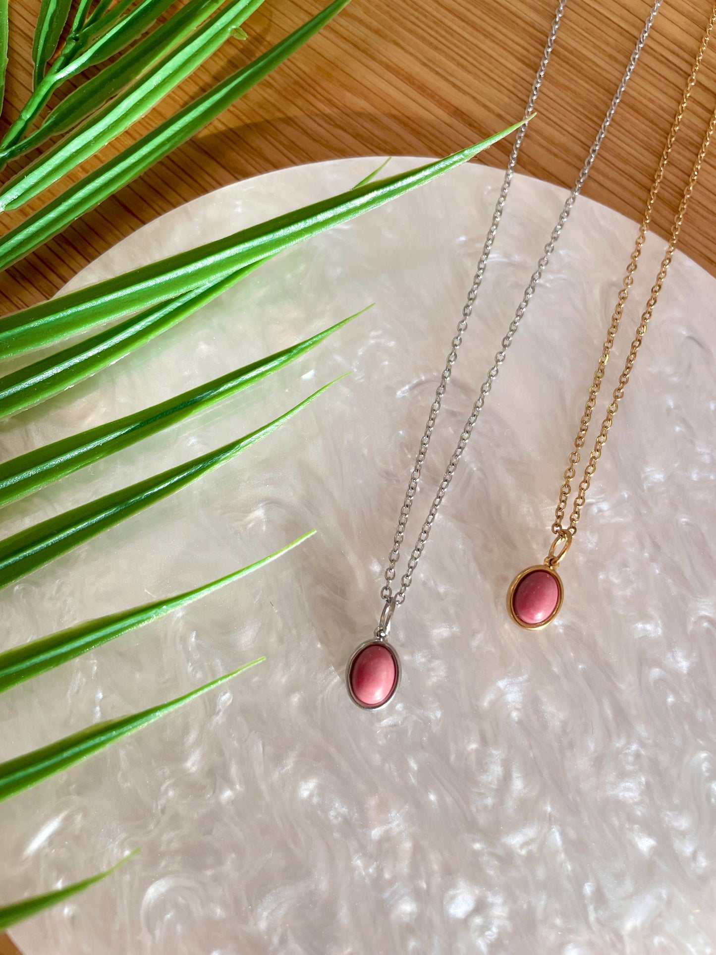 Handgemachte rosa Rhodonit-Ketten mit ovalem Anhänger in Gold und Silber, liegend auf Tablett