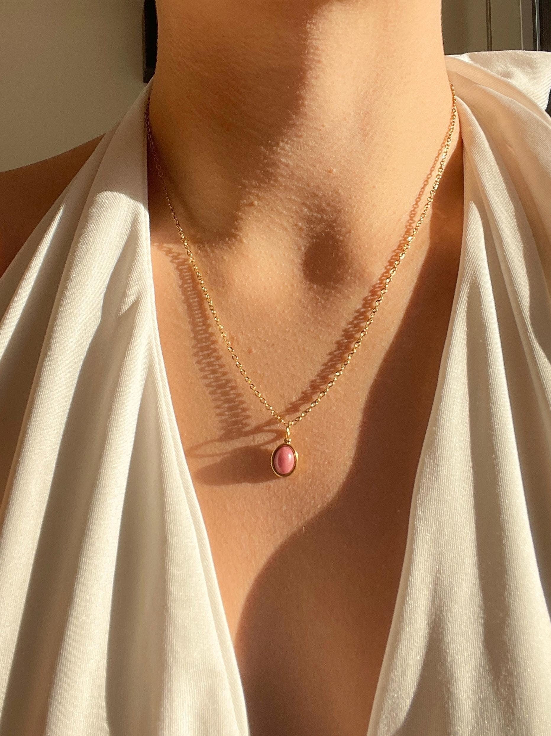 Ovaler rosa Rhodonit-Anhänger an feiner Goldkette, am Hals eines Modells gezeigt in der Sonne
