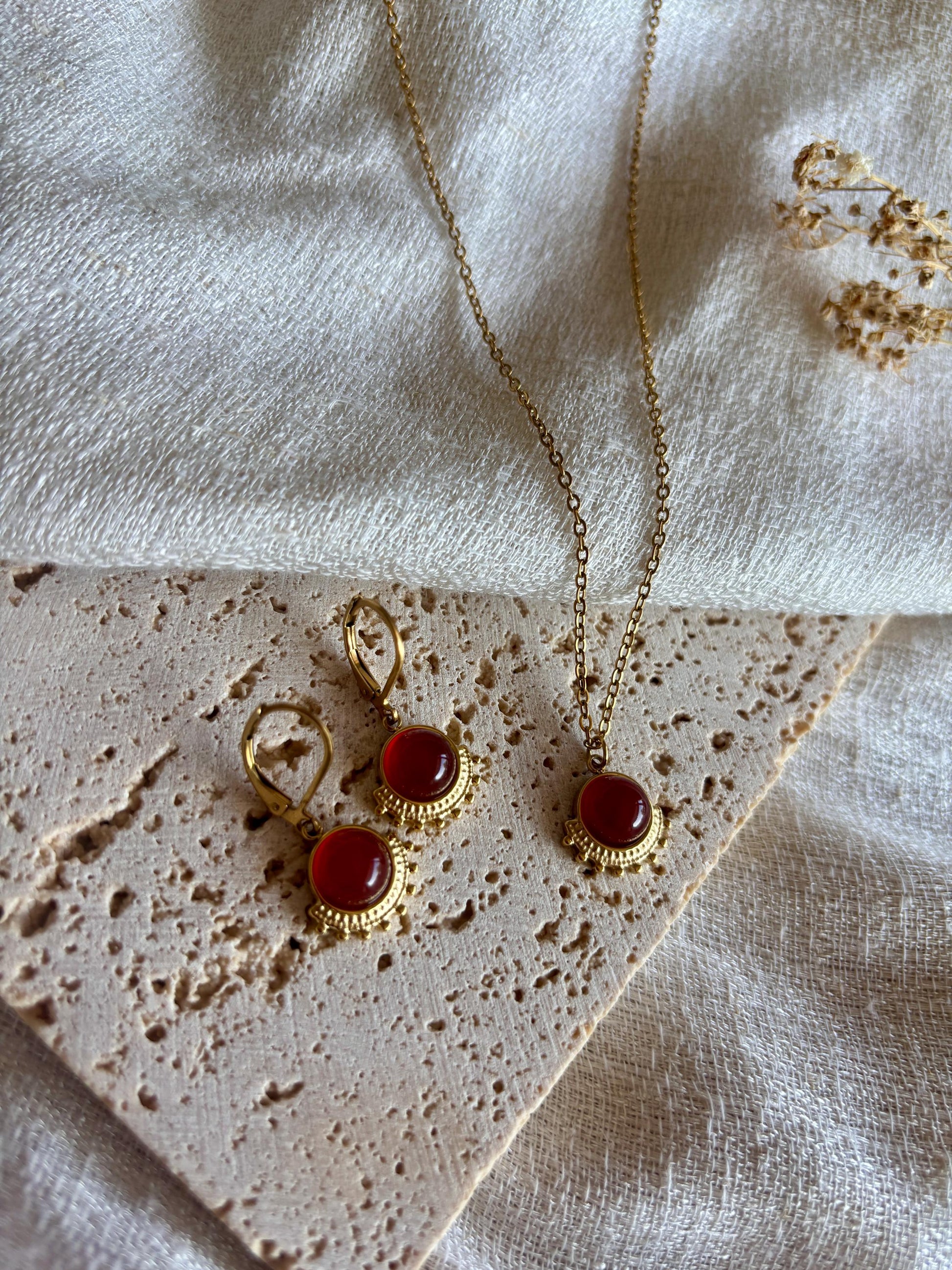 Goldenes Schmuckset mit Ohrringen und Halskette mit roten Karneol Anhängern liegend auf Stein