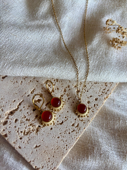 Goldenes Schmuckset mit Ohrringen und Halskette mit roten Karneol Anhängern liegend auf Stein