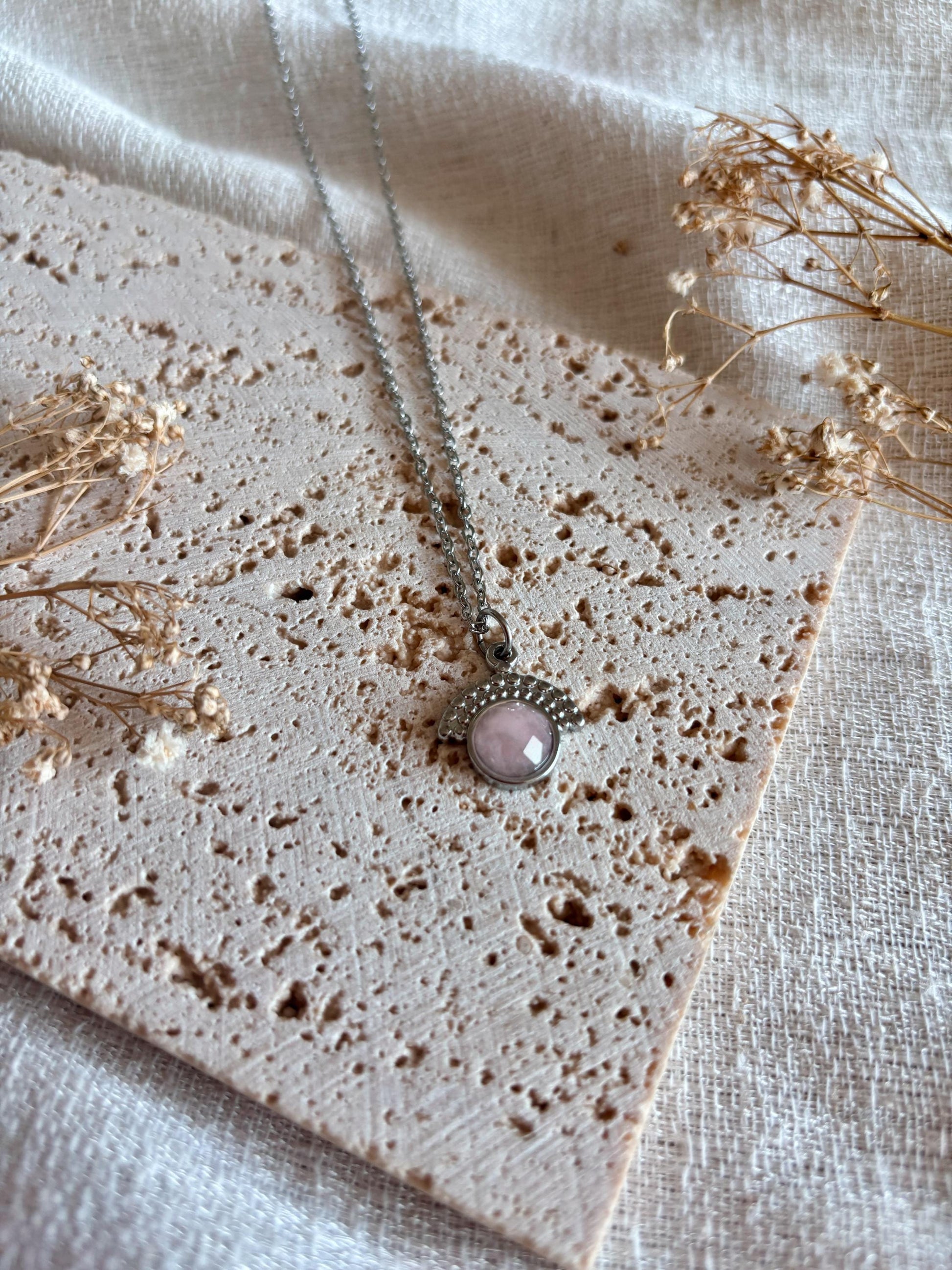 Handgemachte facettierte Rosenquarz-Kette mit rundem Anhänger in Silber,  liegend auf Stein
