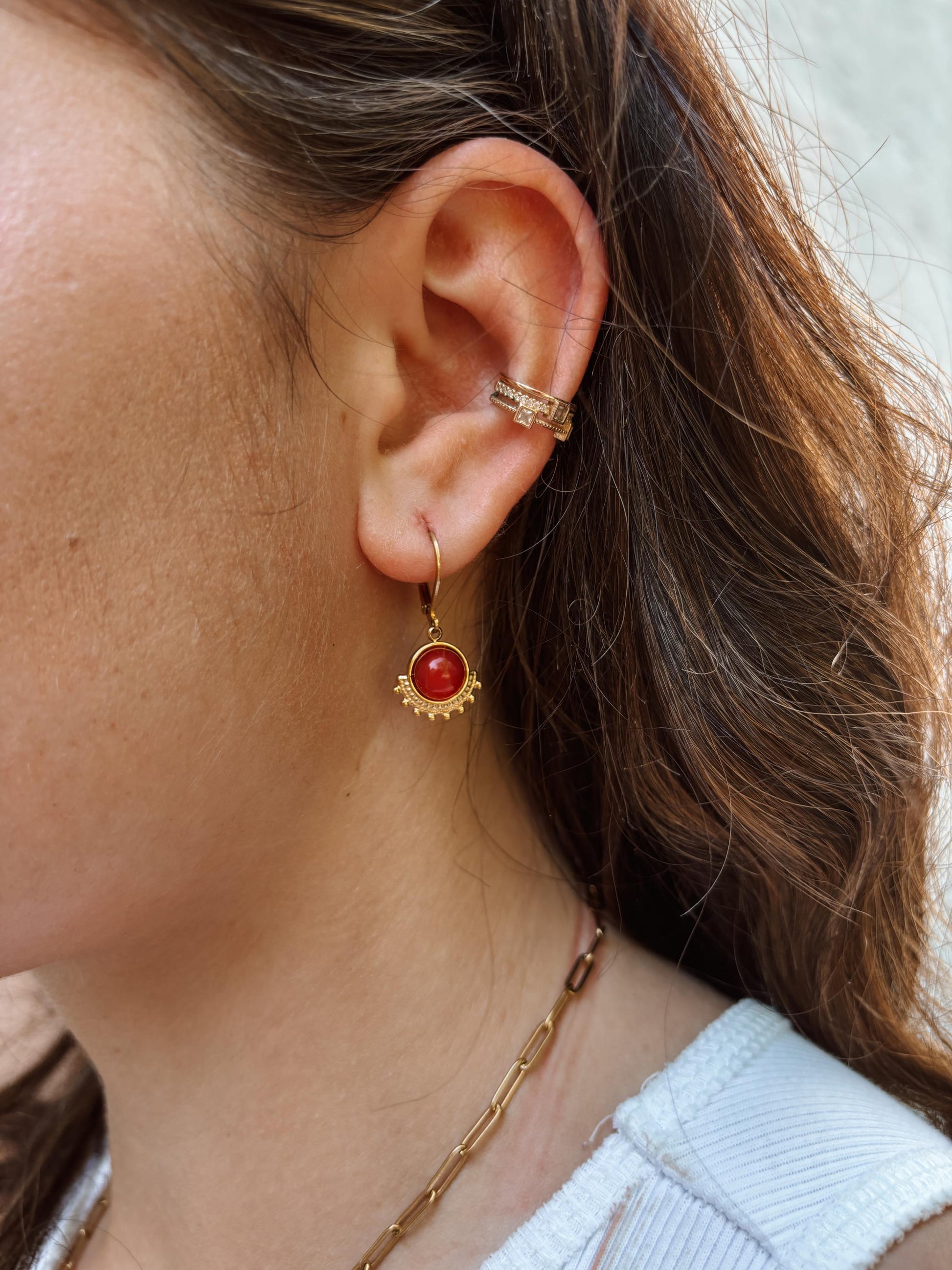 Goldene Creolen-Ohrringe mit Zacken und runden, roten Karneol-Steinen an Ohr eines Modells, Detailaufnahme
