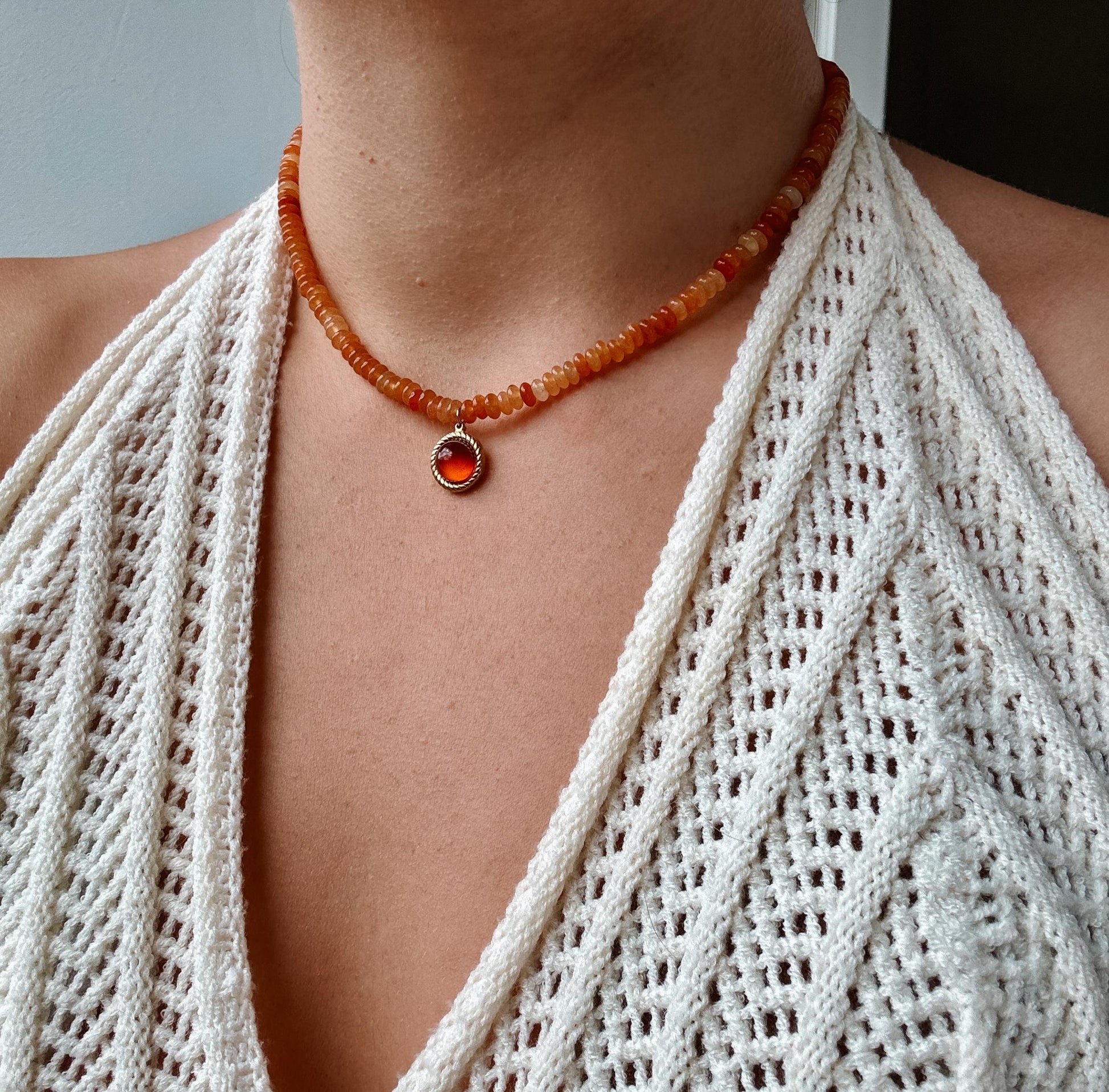 Runder roter Karneol-Anhänger an orangener Karneol Perlen Kette, am Dekolleté eines Modells gezeigt.