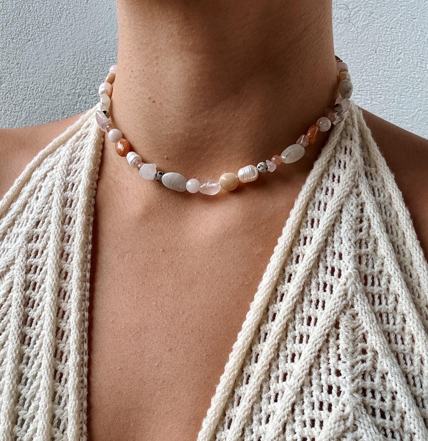 Edelstein-Perlenkette mit Rosenquarz, Mondstein, Sonnenstein und Süßwasserperlen am Dekollete eines Modells mit Häkeltop