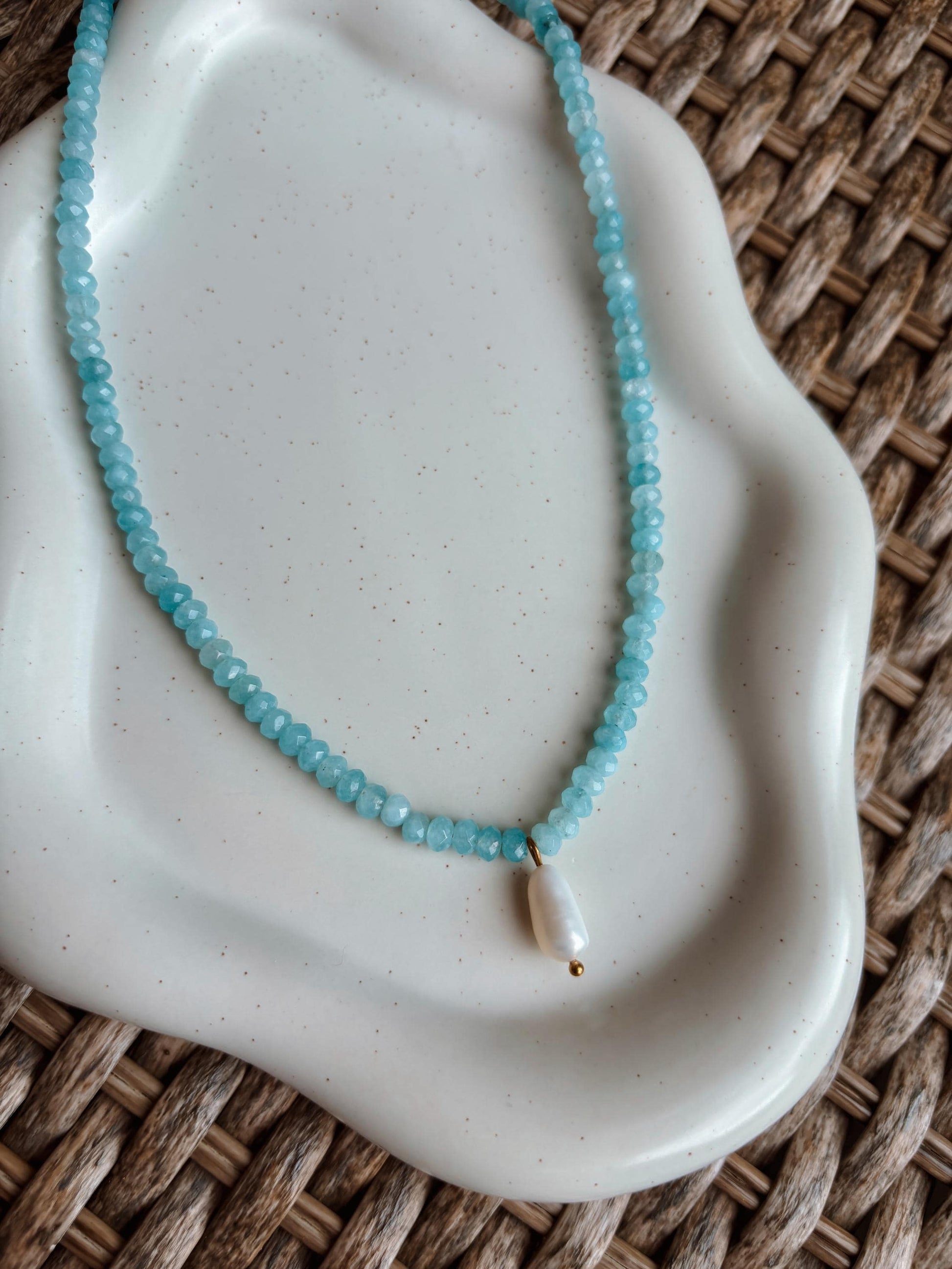 Blaue Jade-Perlenkette mit einem weißen Süßwasserperlen Anhänger liegend auf Steintablett