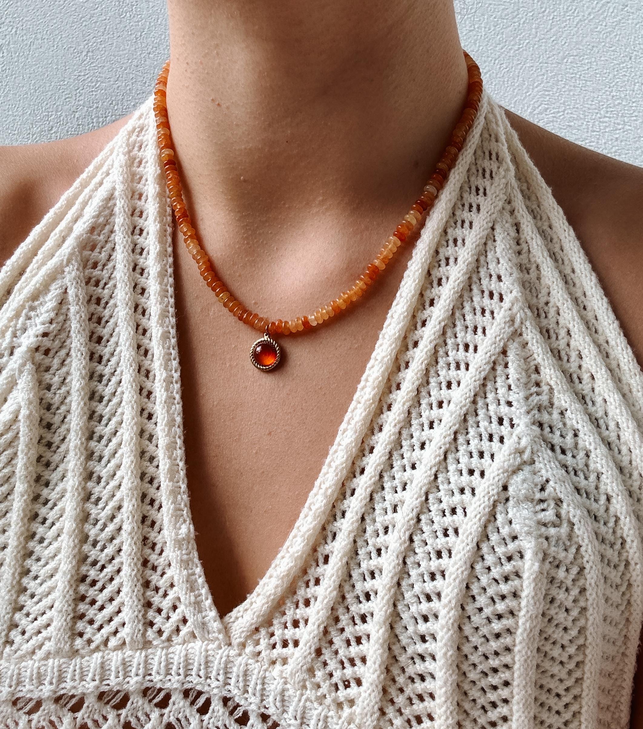 Runder roter Karneol-Anhänger an orangener Perlenkette, am Dekolleté eines Modells gezeigt.
