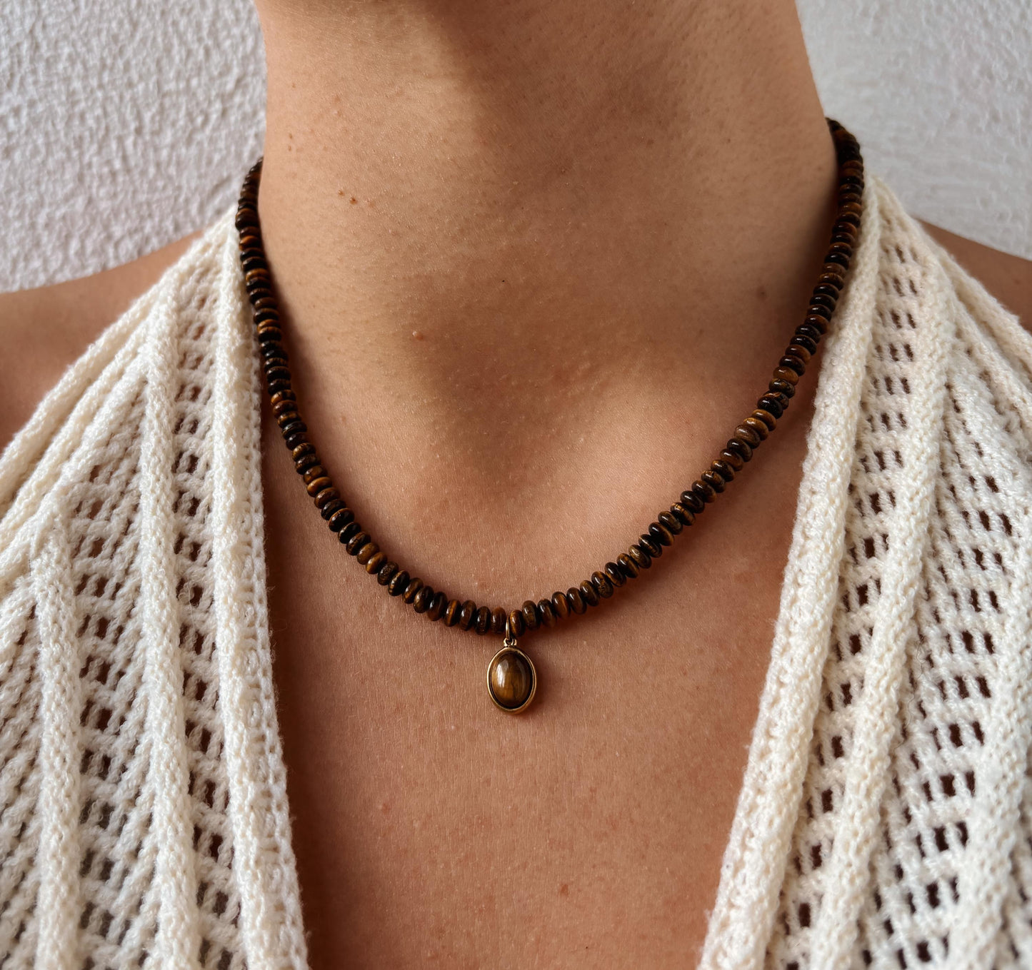 Braune Tigerauge-Perlenkette mit einem ovalen goldenen Tigerauge Anhänger am Hals eines Modells mit Häkeltop