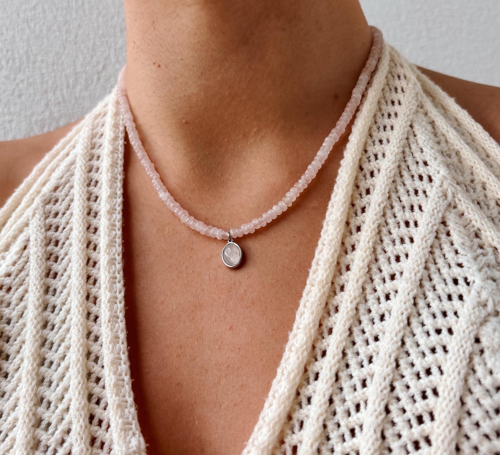 Rosenquarz-Perlenkette mit einem ovalen silbernen Rosenquarz Anhänger am Hals eines Modells mit Häkeltop