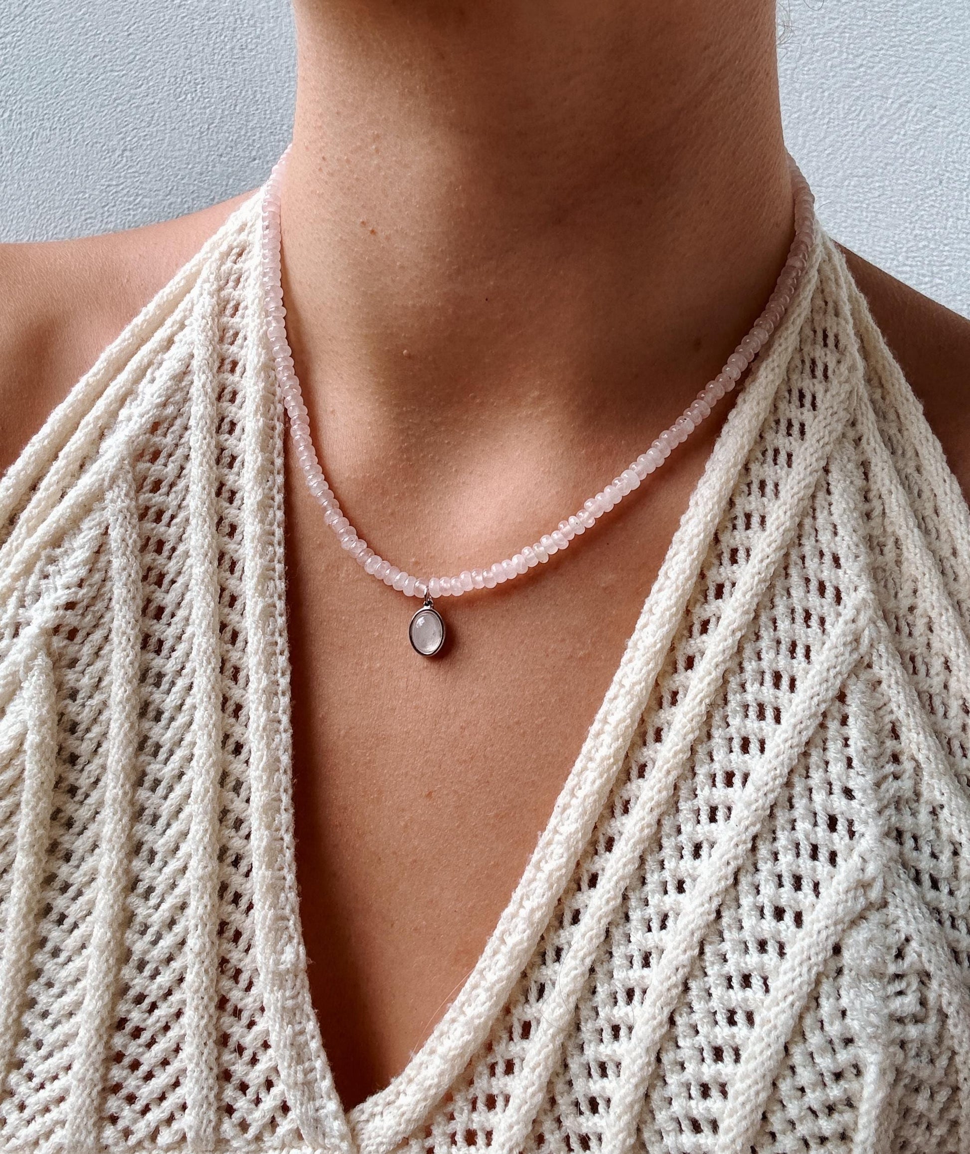 Rosenquarz-Perlenkette mit einem ovalen silbernen Rosenquarz Anhänger am Dekollete eines Modells mit Häkeltop