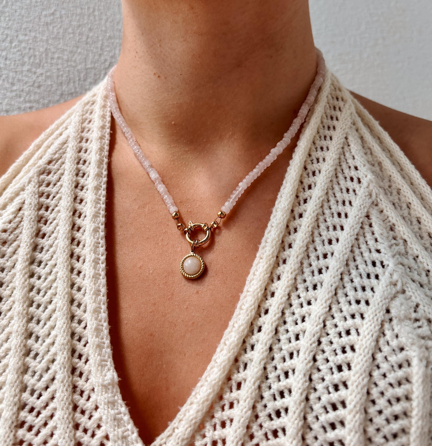 Rosenquarz-Perlenkette mit einem runden goldenen Rosenquarz Anhänger am Dekollete eines Modells mit Häkeltop