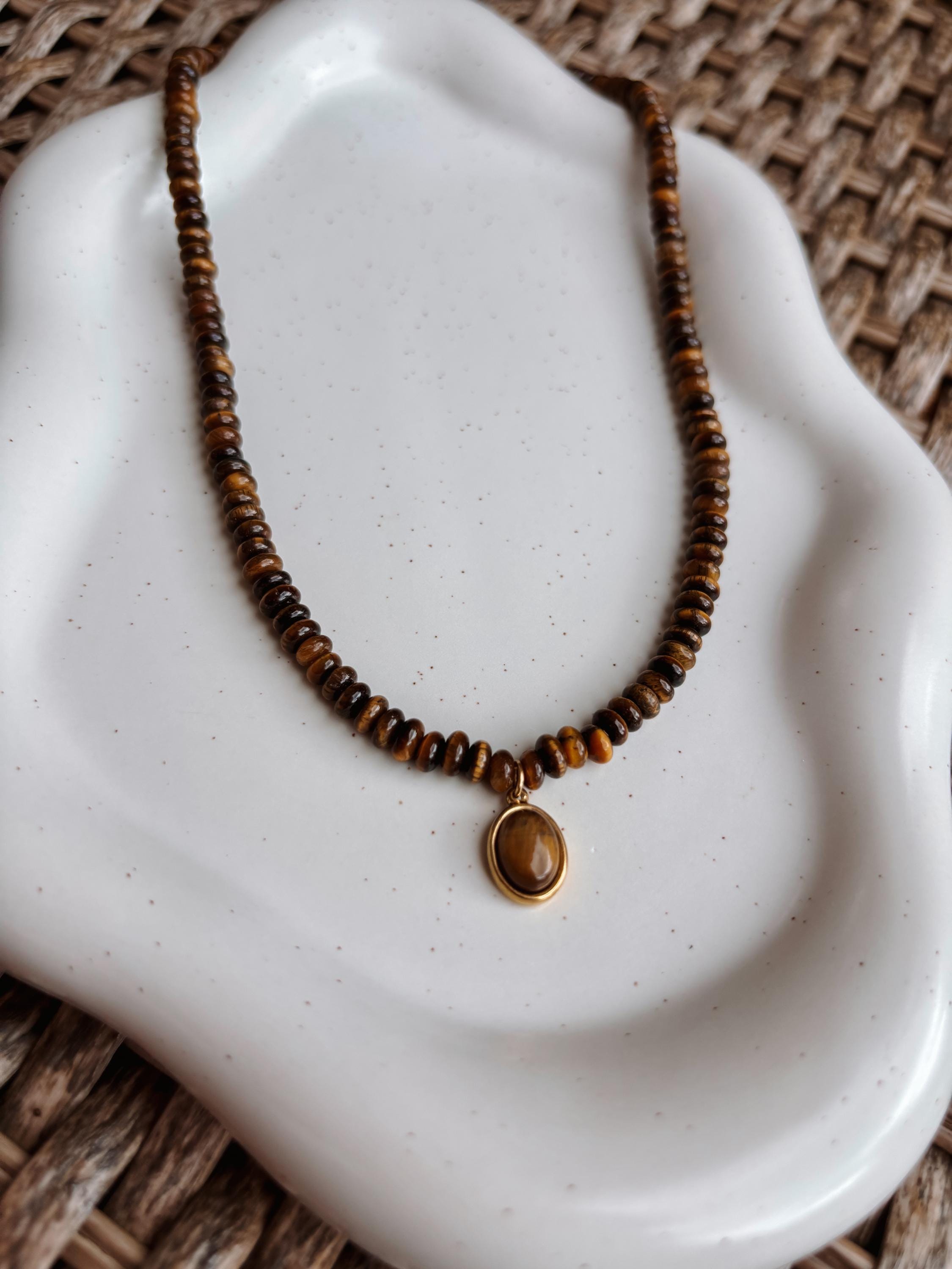 Braune Tigerauge-Perlenkette mit einem ovalen goldenen Tigerauge Anhänger liegend auf Tablett, Detailaufnahme