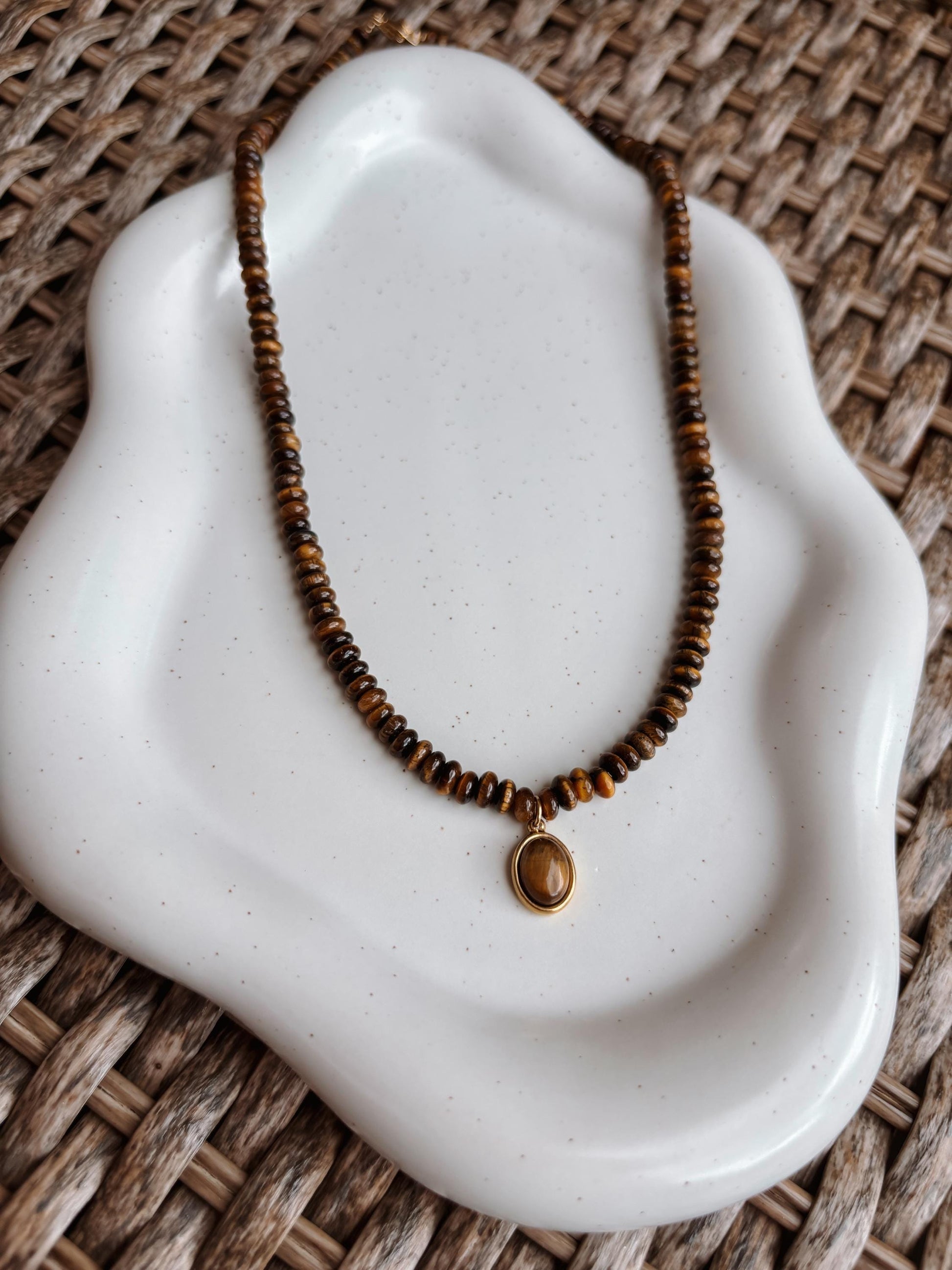 Braune Tigerauge-Perlenkette mit einem ovalen goldenen Tigerauge Anhänger liegend auf Tablett