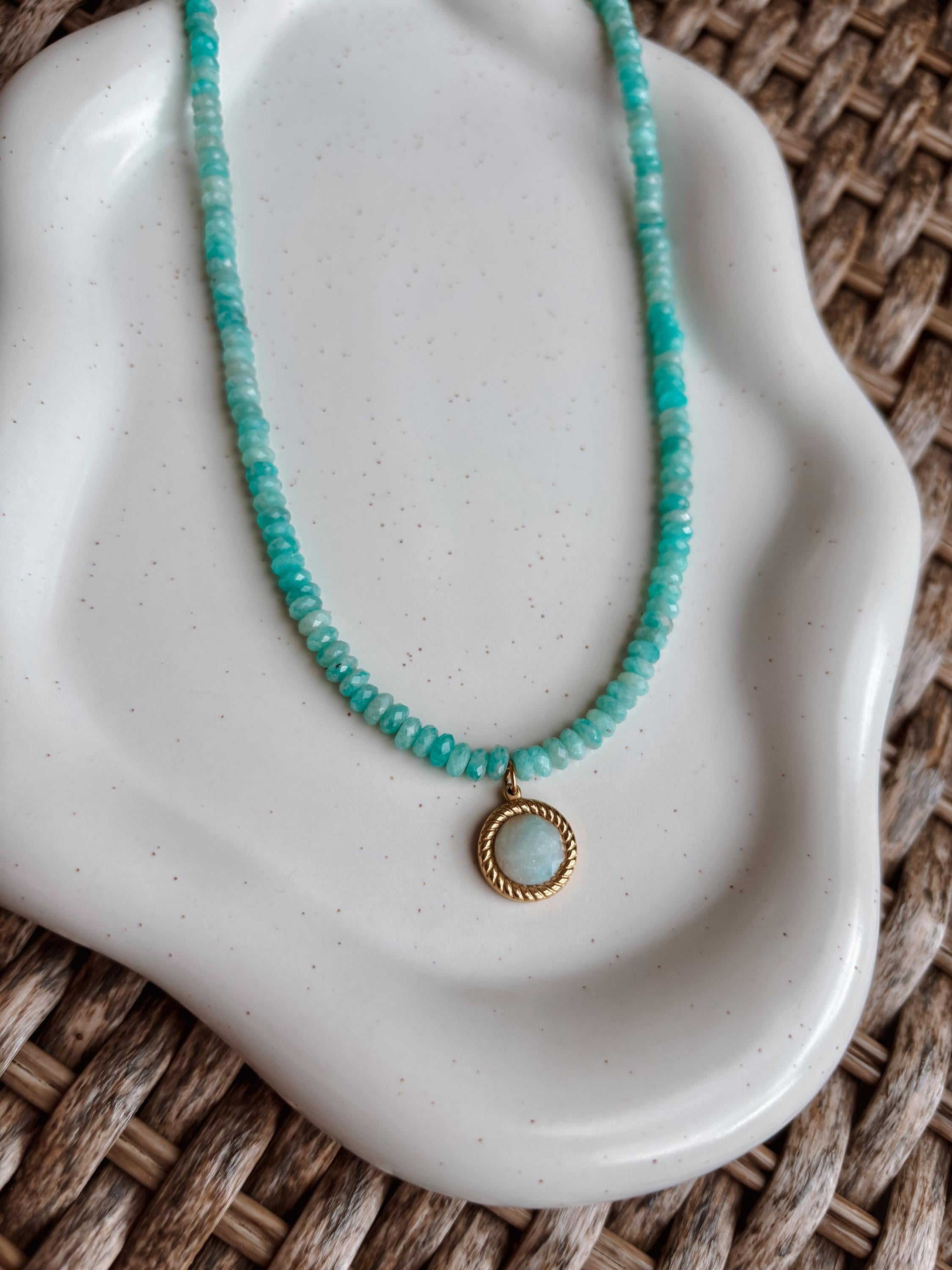 Blaue Amazonit-Perlenkette mit einem runden facettierten Amazonit Anhänger in Gold liegend auf Tablett