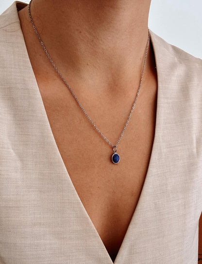 Halskette mit rundem Lapislazuli-Anhänger an einer Person mit beigefarbenem Oberteil.