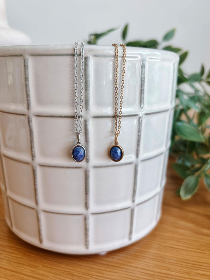 Zwei Paar Lapislazuli-Ohrringe mit Silber- und Goldketten hängen an einem weißen Keramiktopf.
