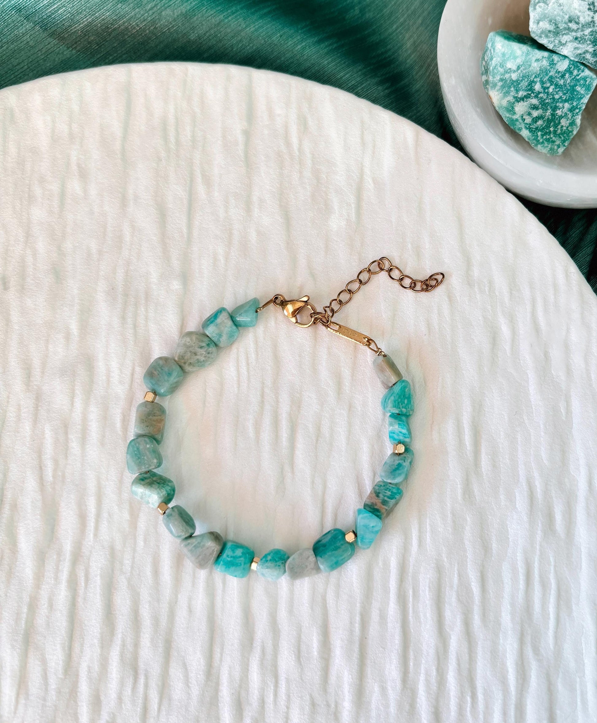 Goldenes Amazonit Perlenarmband mit türkisen Natursteinen liegend auf weißem Tablett, Ansicht von oben
