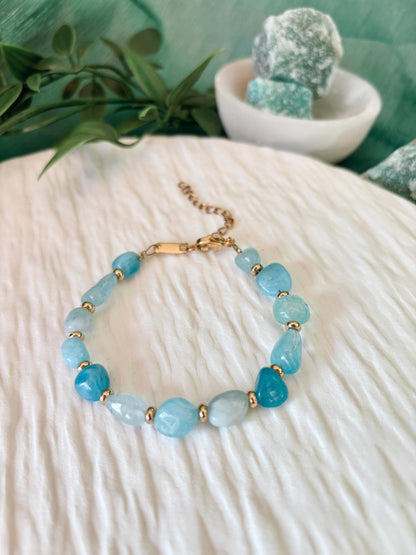Goldenes Aquamarin Perlenarmband mit blauen Natursteinen liegend auf weißem Tablett, Frontalsicht