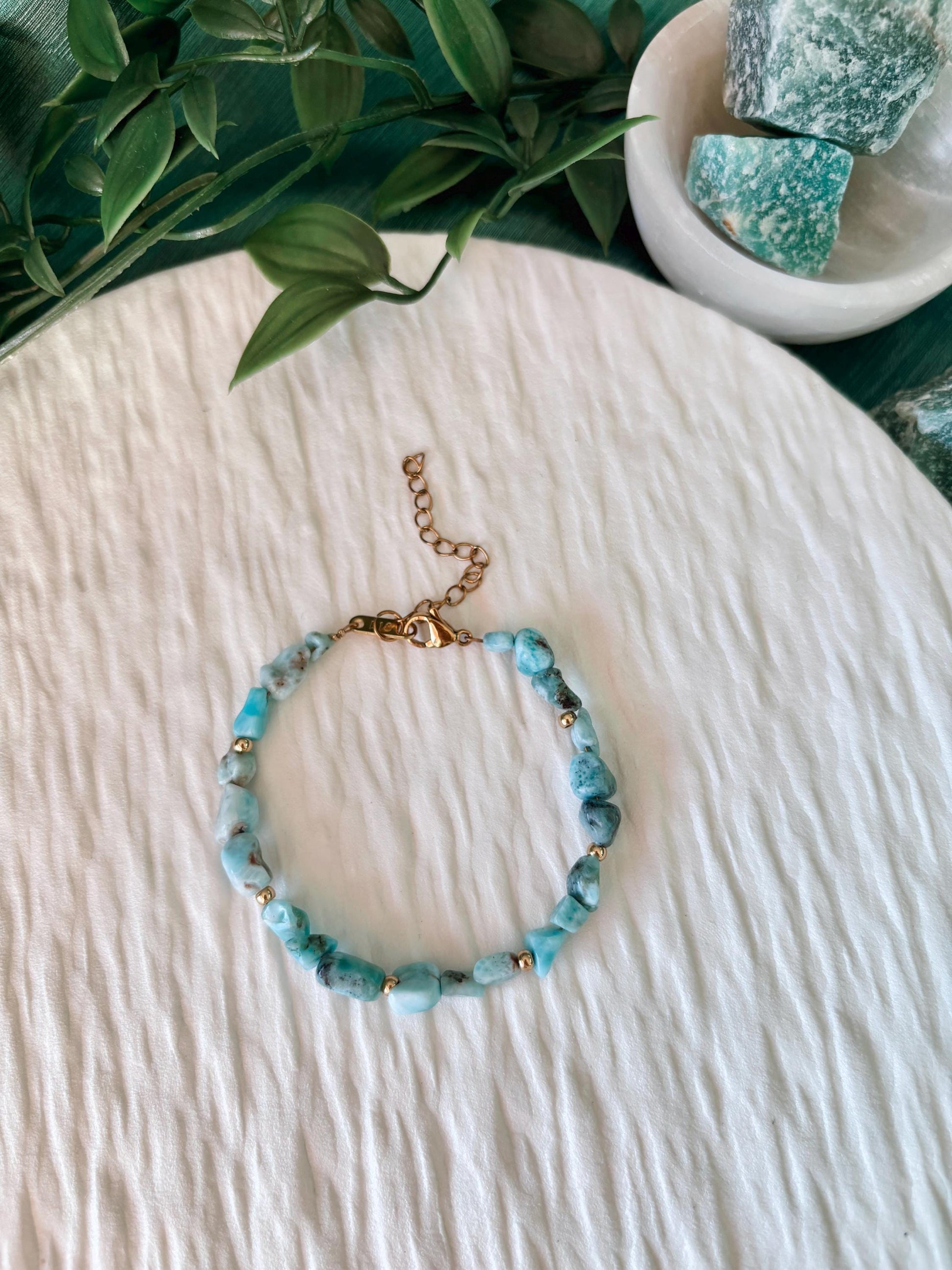 Goldenes Larimar Perlenarmband mit blauen Natursteinen liegend auf weißem Tablett, Ansicht von oben