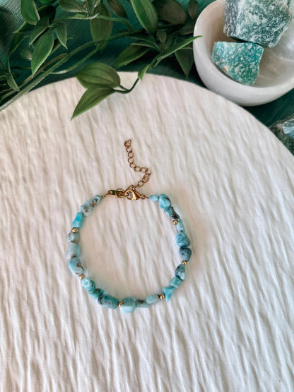 Goldenes Larimar Perlenarmband mit blauen Natursteinen liegend auf weißem Tablett, Ansicht von oben