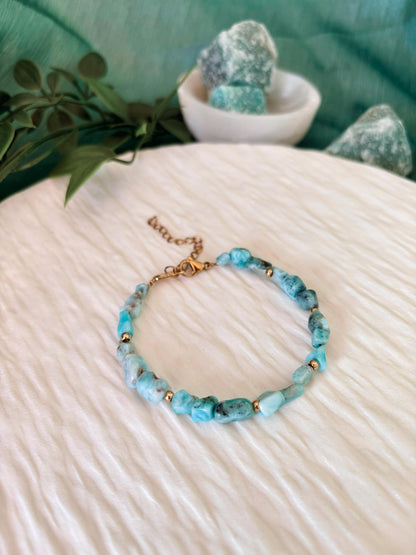 Goldenes Larimar Perlenarmband mit blauen Natursteinen liegend auf weißem Tablett, Ansicht von vorne