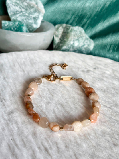 Sonnenstein-Armband Pearl auf hellem Untergrund vor grünem Hintergrund mit Steinen im Hintergrund.