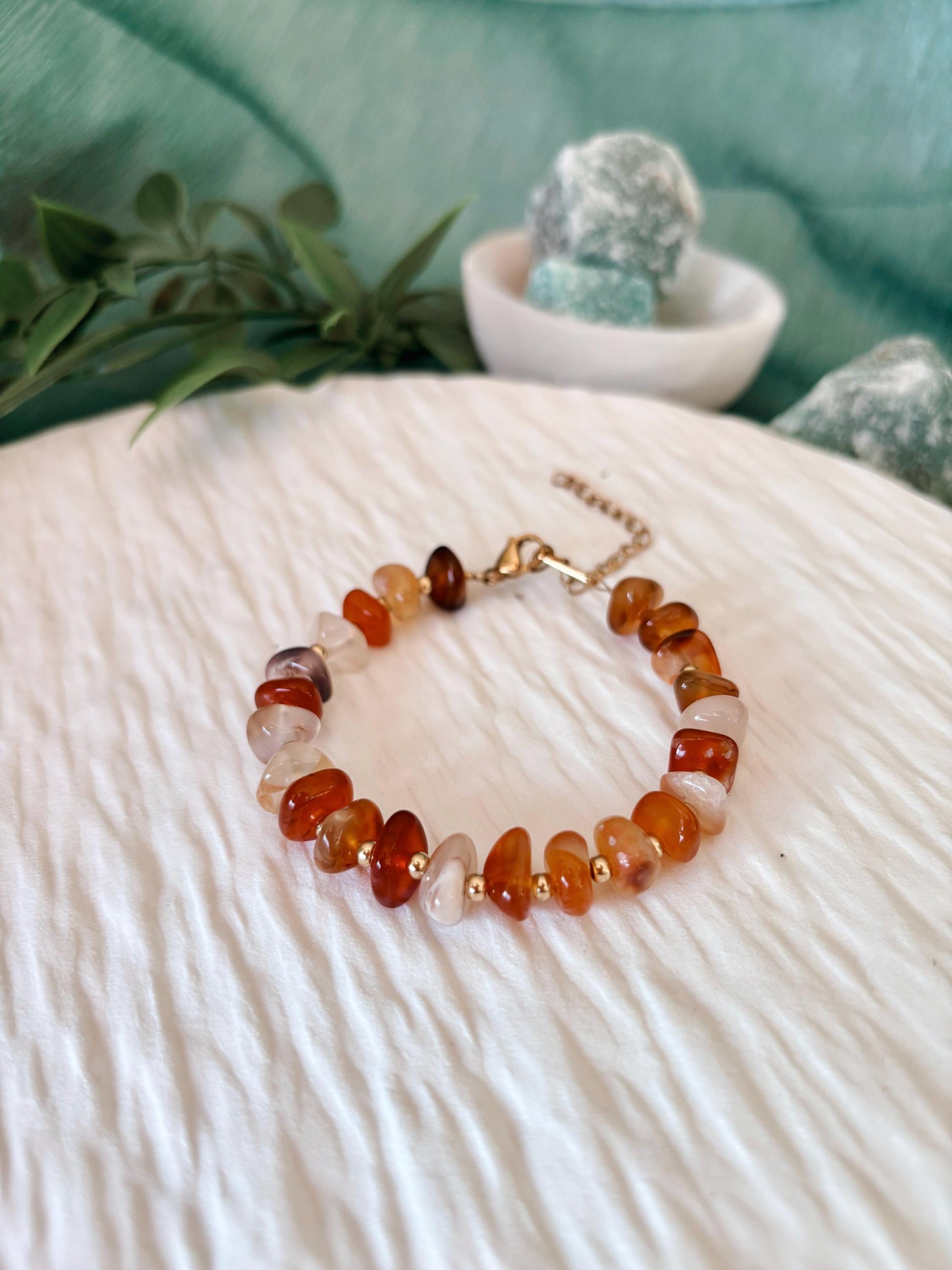 Goldenes Karneol Perlenarmband mit rot-orangenen Natursteinen liegend auf weißem Tablett, Ansicht von vorne