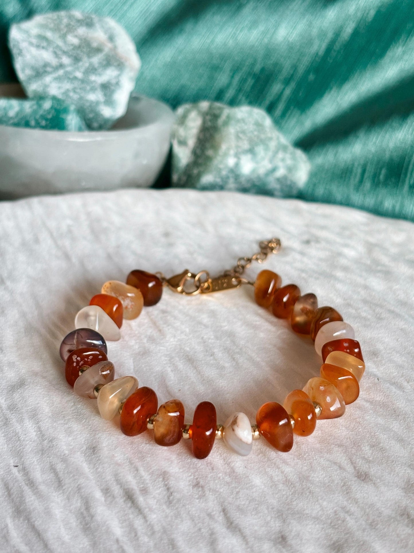 Goldenes Karneol Perlenarmband mit roten Natursteinen liegend auf weißem Tablett, Detailaufnahme
