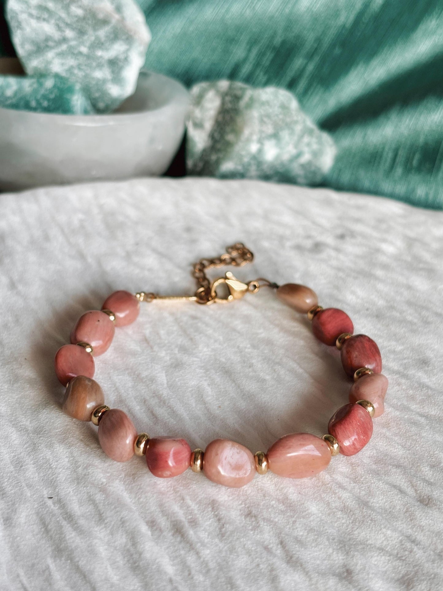 Goldenes Rhodonit Perlenarmband mit rosa Natursteinen liegend auf weißem Tablett, Detailaufnahme