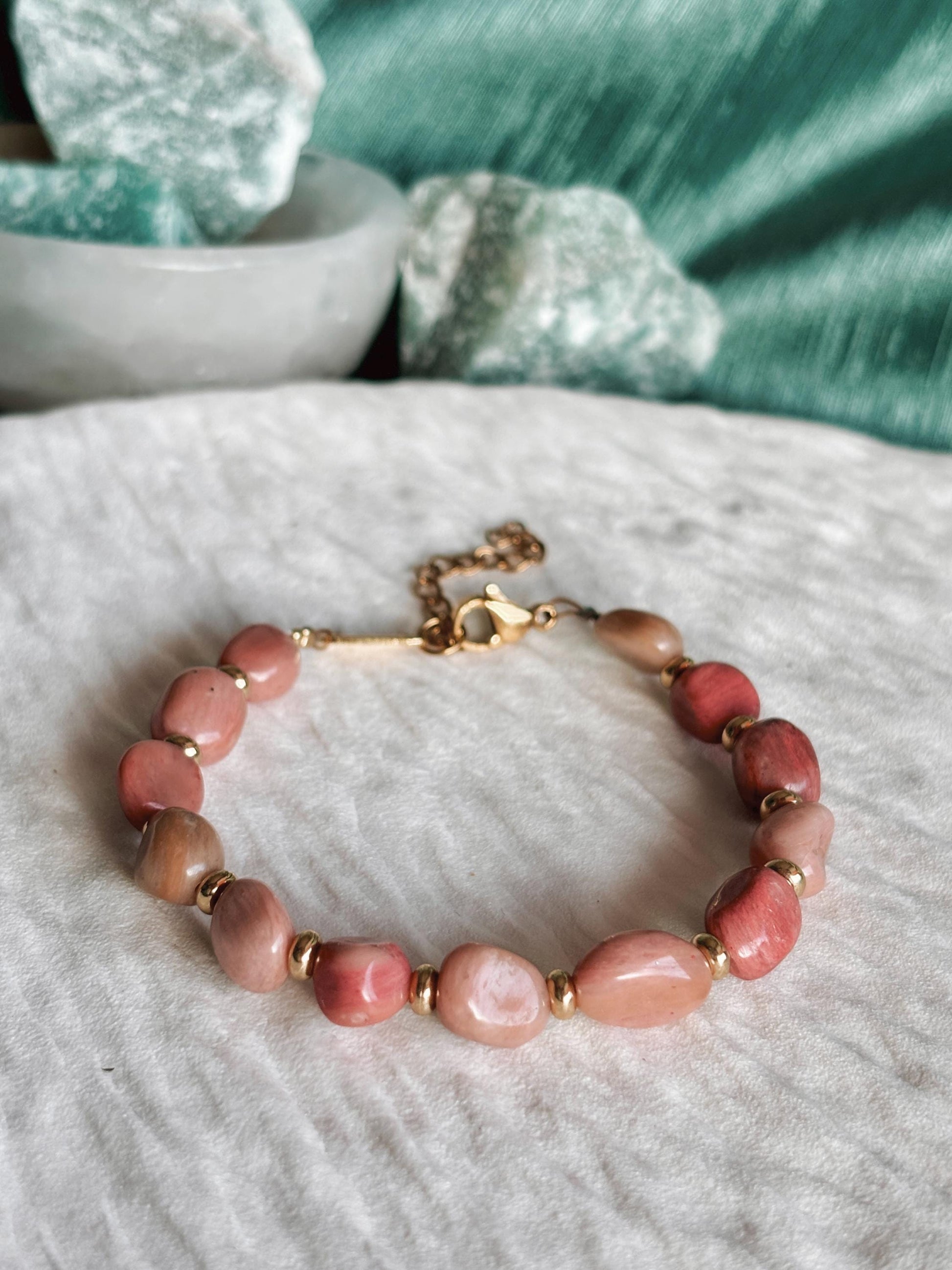 Goldenes Rhodonit Perlenarmband mit rosa Natursteinen liegend auf weißem Tablett, Detailaufnahme