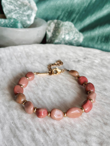 Goldenes Rhodonit Perlenarmband mit rosa Natursteinen liegend auf weißem Tablett, Detailaufnahme