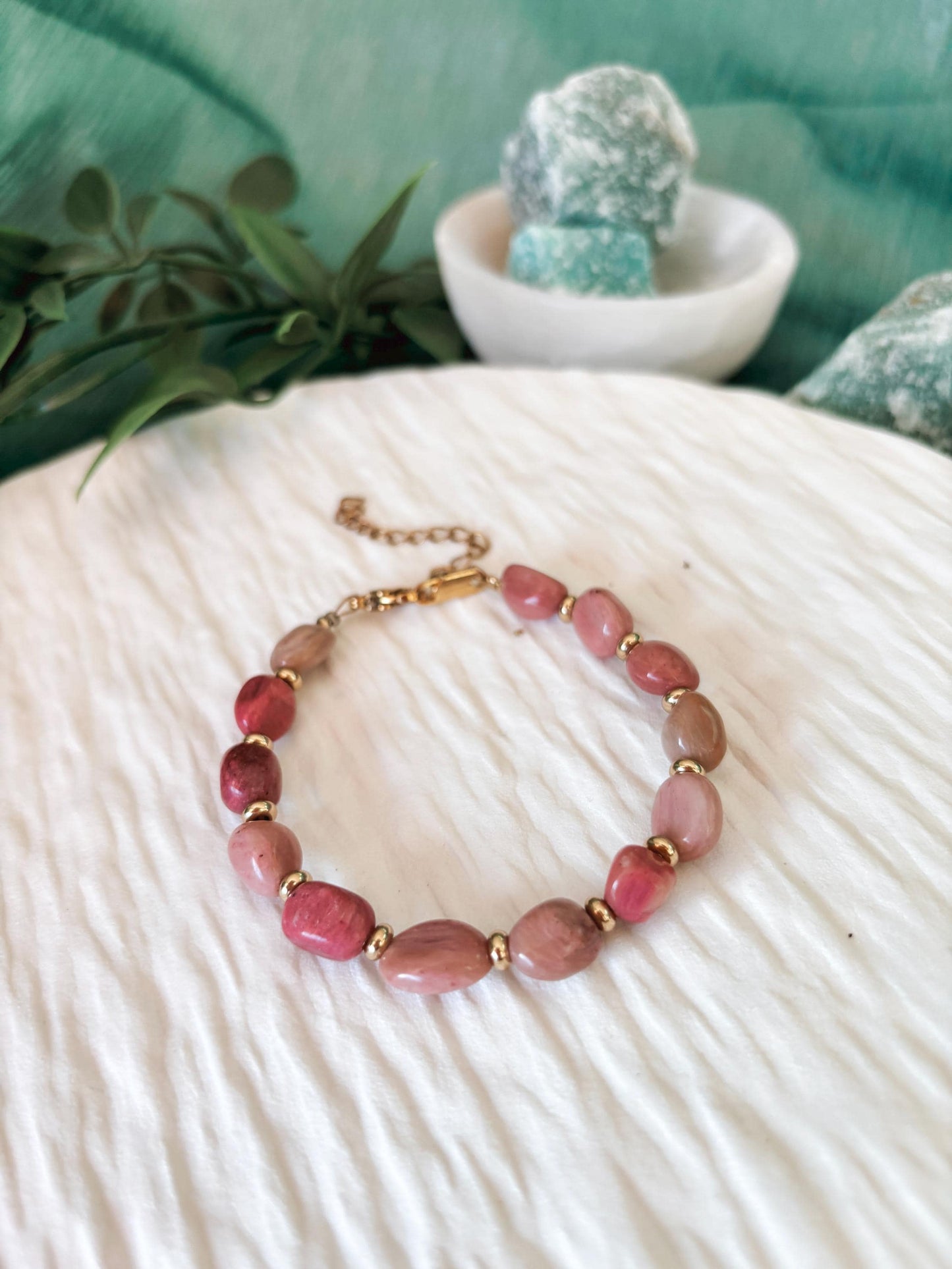 Goldenes Rhodonit Perlenarmband mit pinken Natursteinen liegend auf weißem Tablett, Ansicht von vorne
