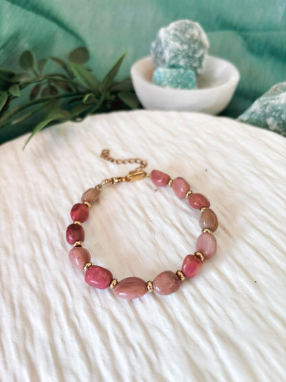 Goldenes Rhodonit Perlenarmband mit pinken Natursteinen liegend auf weißem Tablett, Ansicht von vorne