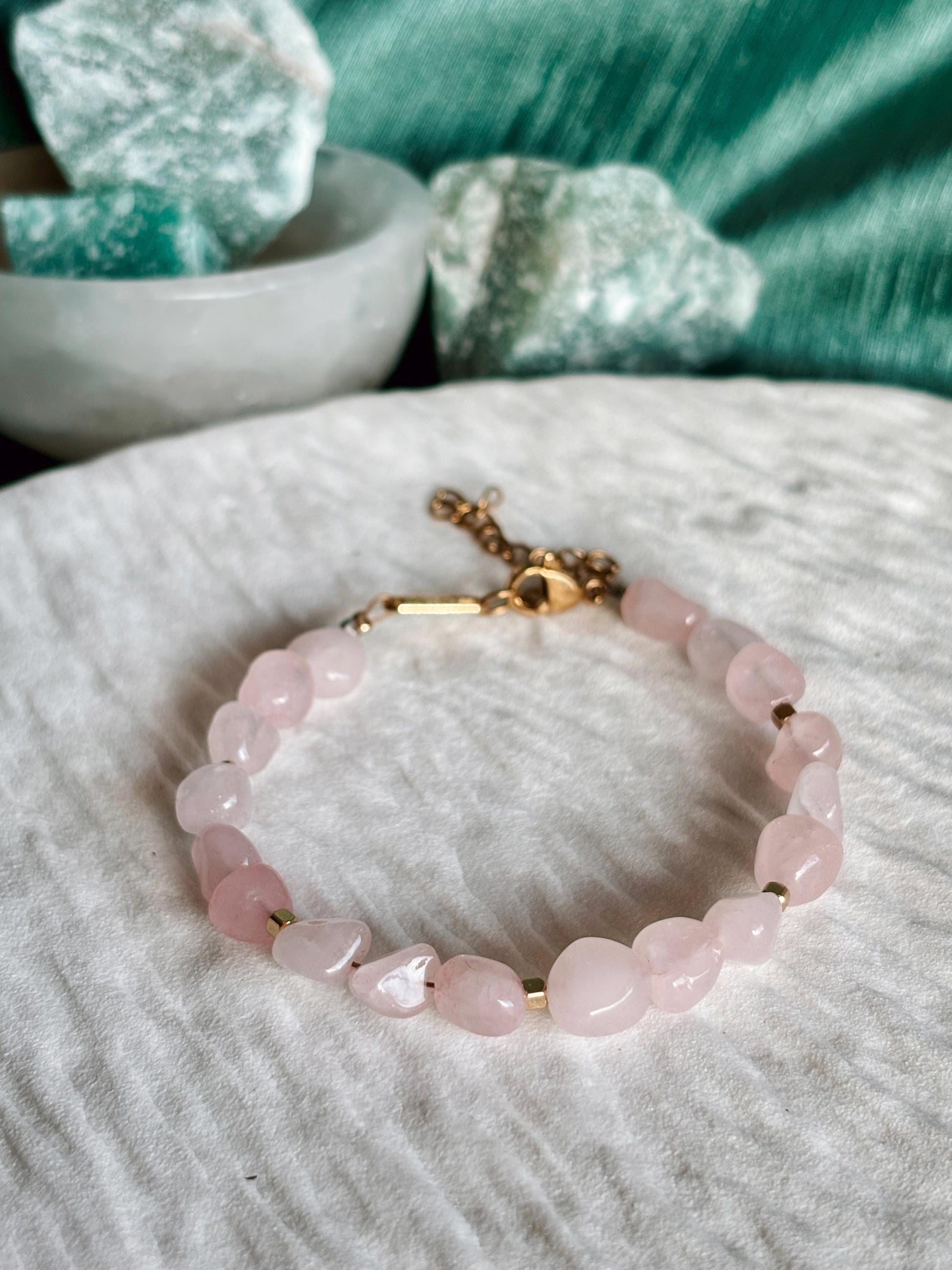 Goldenes Rosenquarz Perlenarmband mit rosa Natursteinen liegend auf weißem Tablett, Detailaufnahme