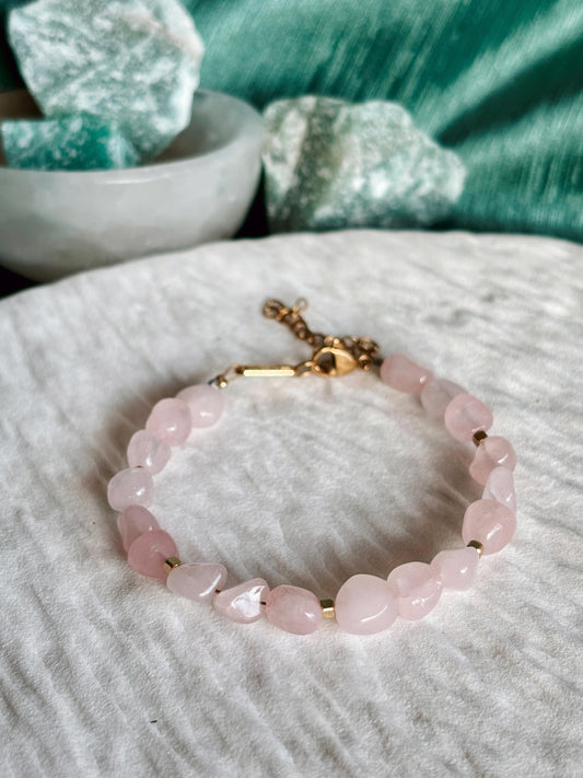 Goldenes Rosenquarz Perlenarmband mit rosa Natursteinen liegend auf weißem Tablett, Detailaufnahme