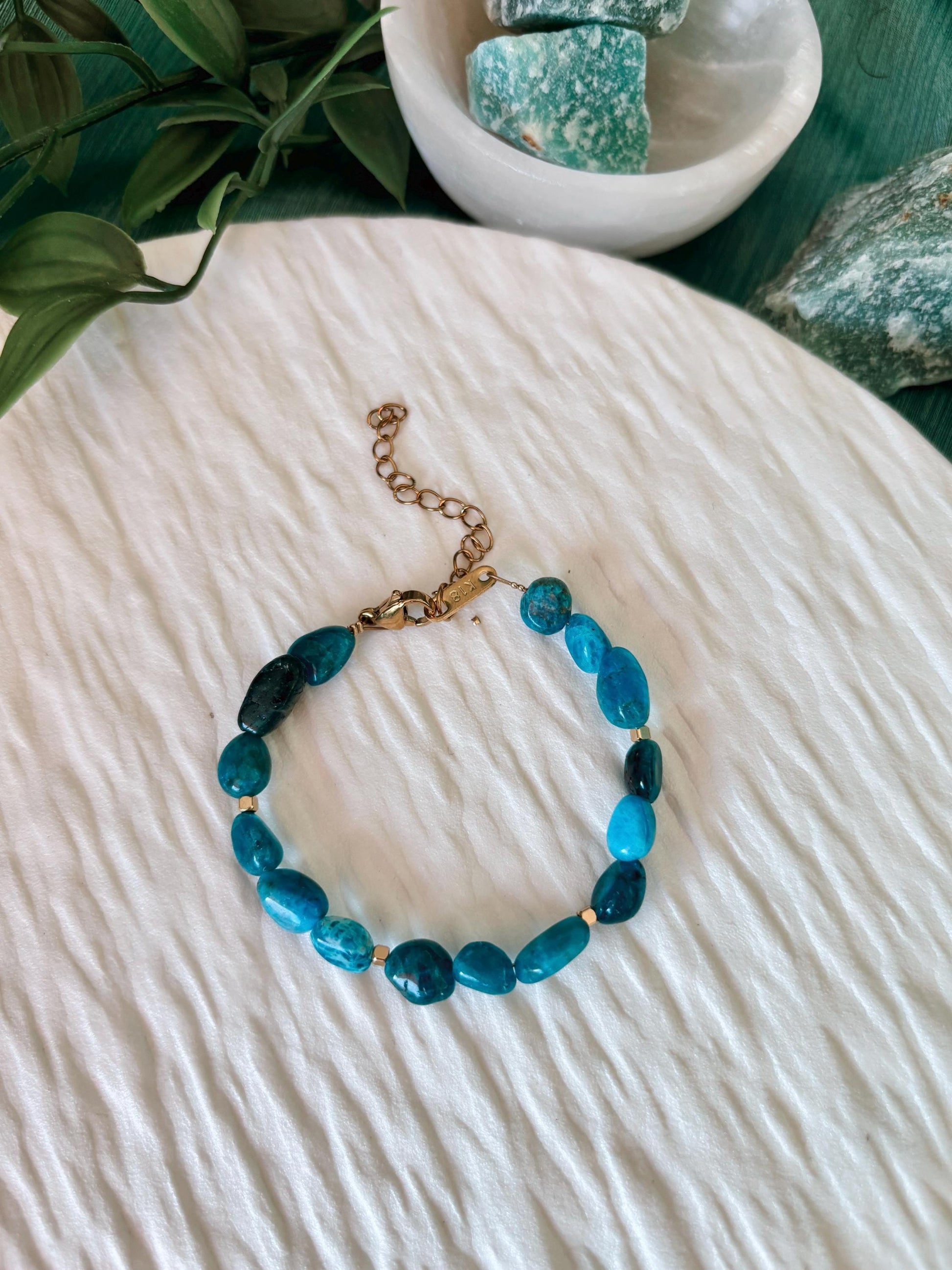 Goldenes Apatit Perlenarmband mit blauen Natursteinen liegend auf weißem Tablett, Ansicht von oben